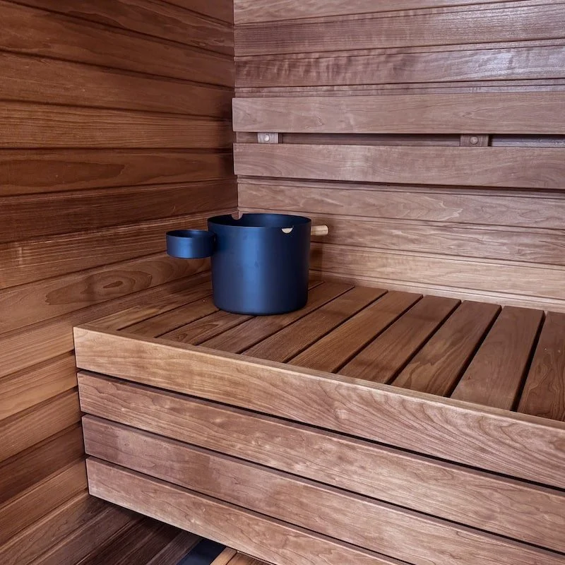 A blue sauna bucket with a wooden handle inside a wooden sauna room.