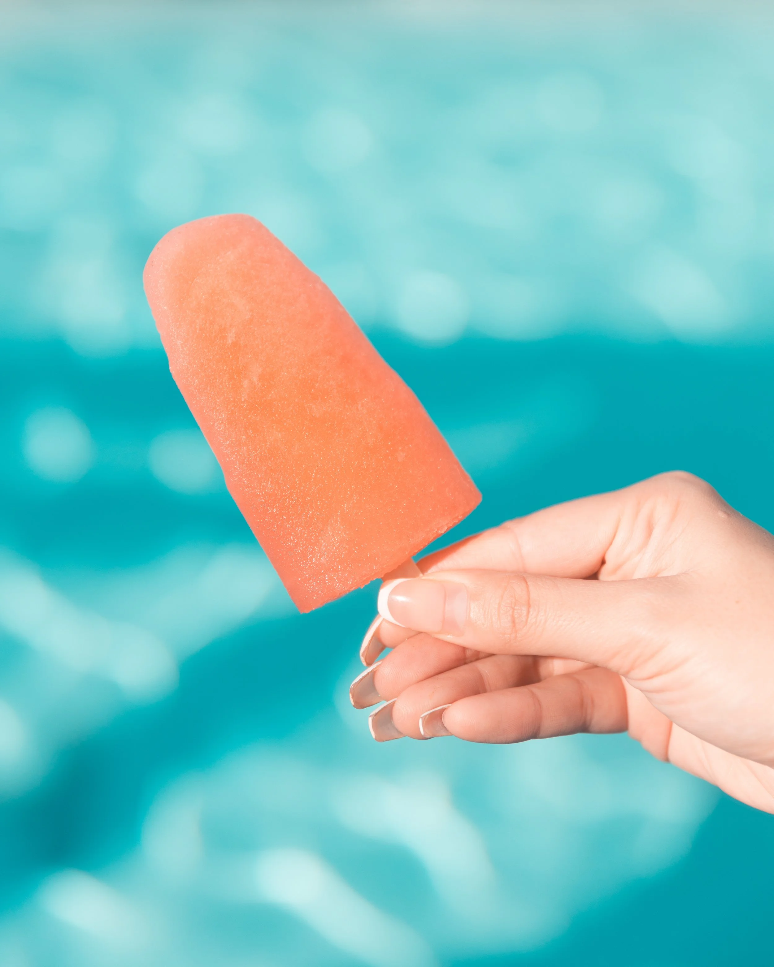 Person holding a pink popsicle against a blurred blue background.