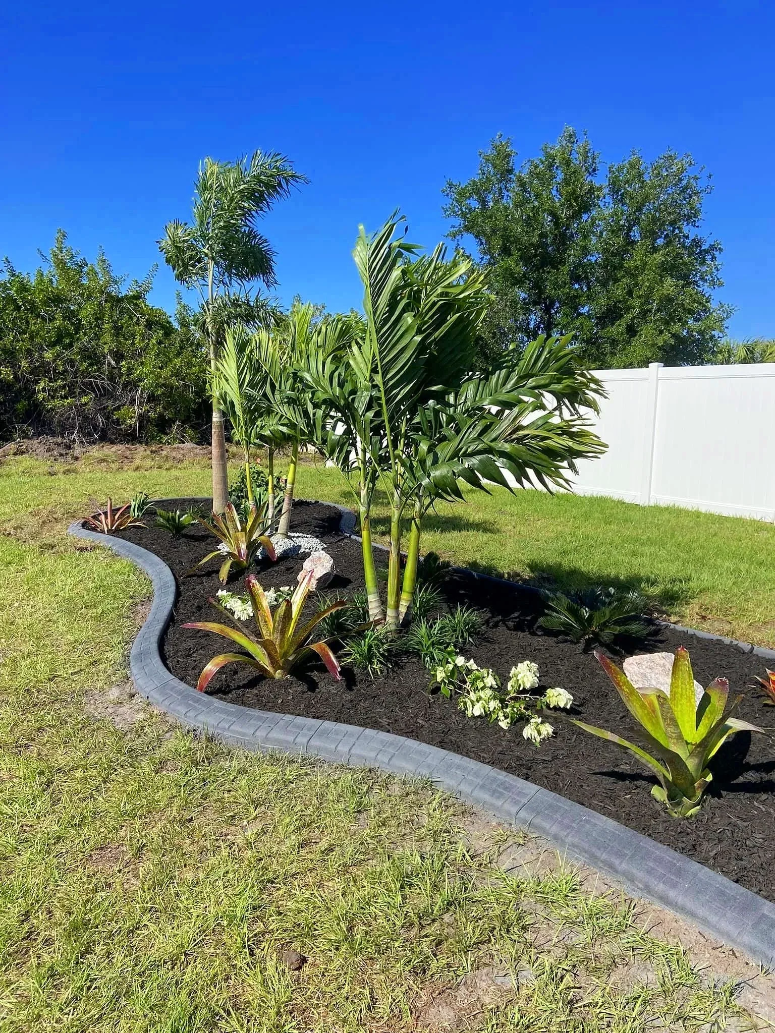 Backyard island installed with concrete curbing, mulch, palm trees, and plants at home in Rotonda West by LD Lifestyles.