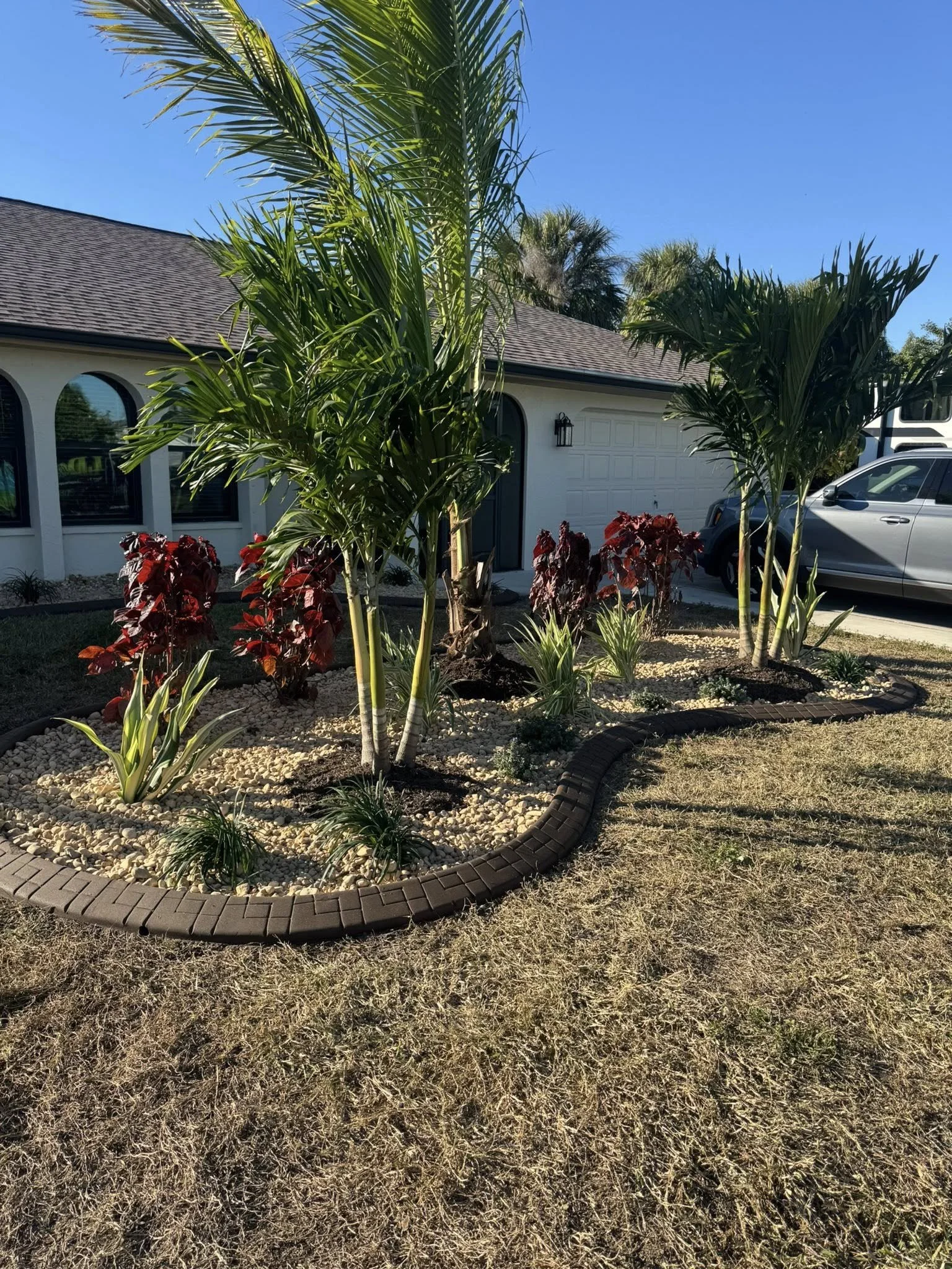 Front yard tropical landscape designed with rocks, curbing, trees installed by LD Lifestyles in Port Charlotte Florida.