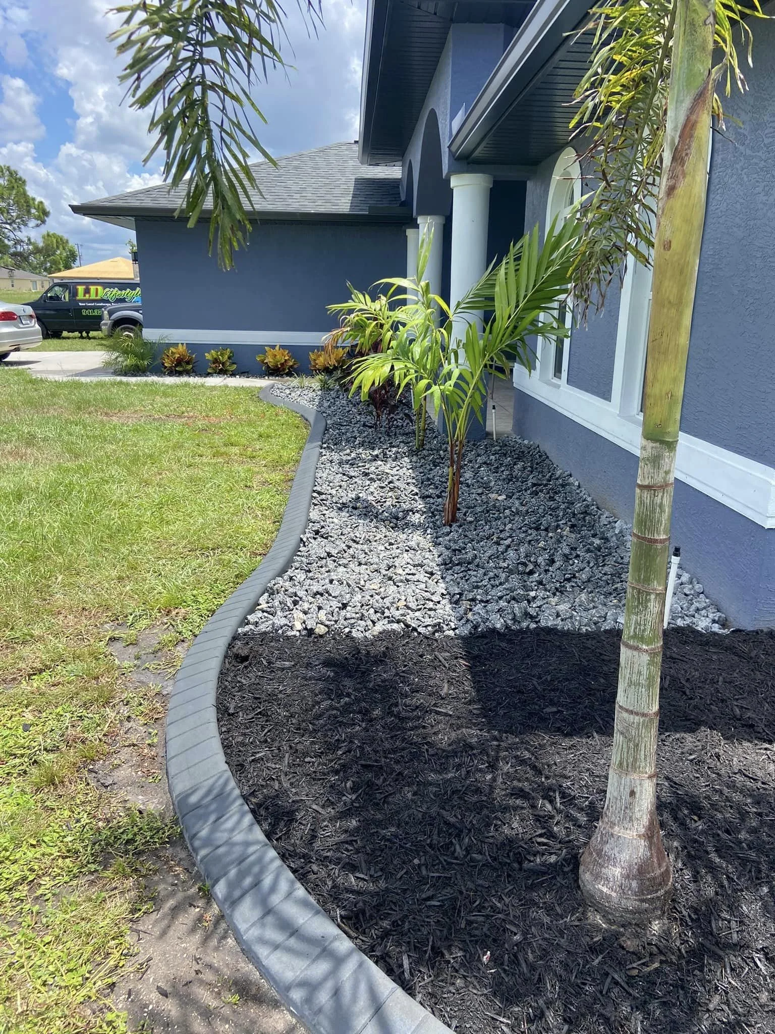 Front yard landscape design with rock, mulch, palms, low maintenance plants, and concrete curbing at Port Charlotte home by LD Lifestyles.
