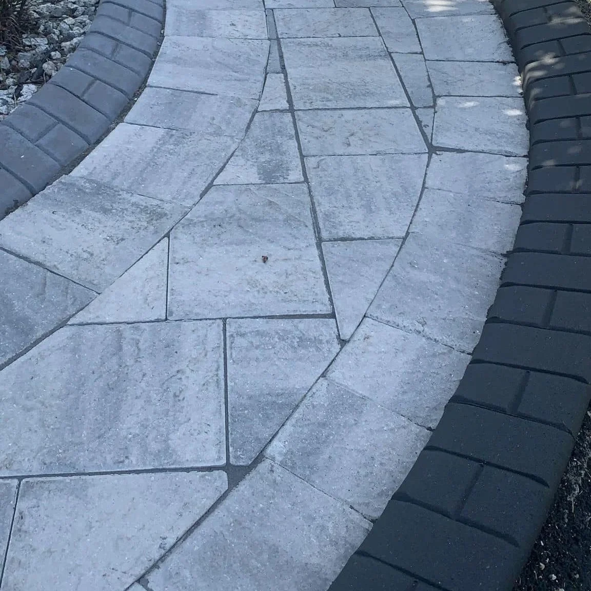 Close-up view of a paved walkway made of large, irregularly shaped stone tiles, bordered on each side by a row of dark gray bricks.