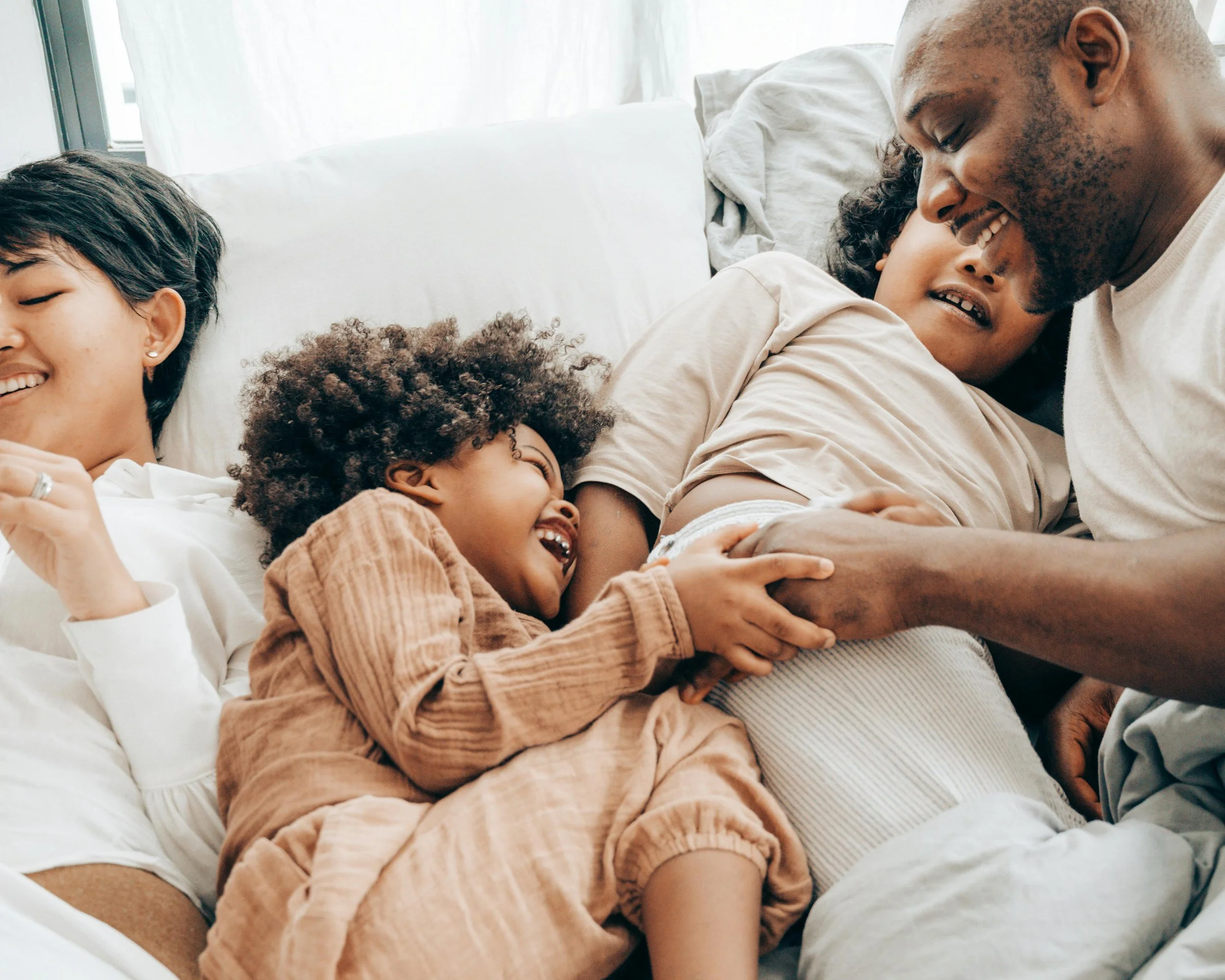 Family lying on a bed, smiling and laughing together, with parents and children enjoying a joyful moment.