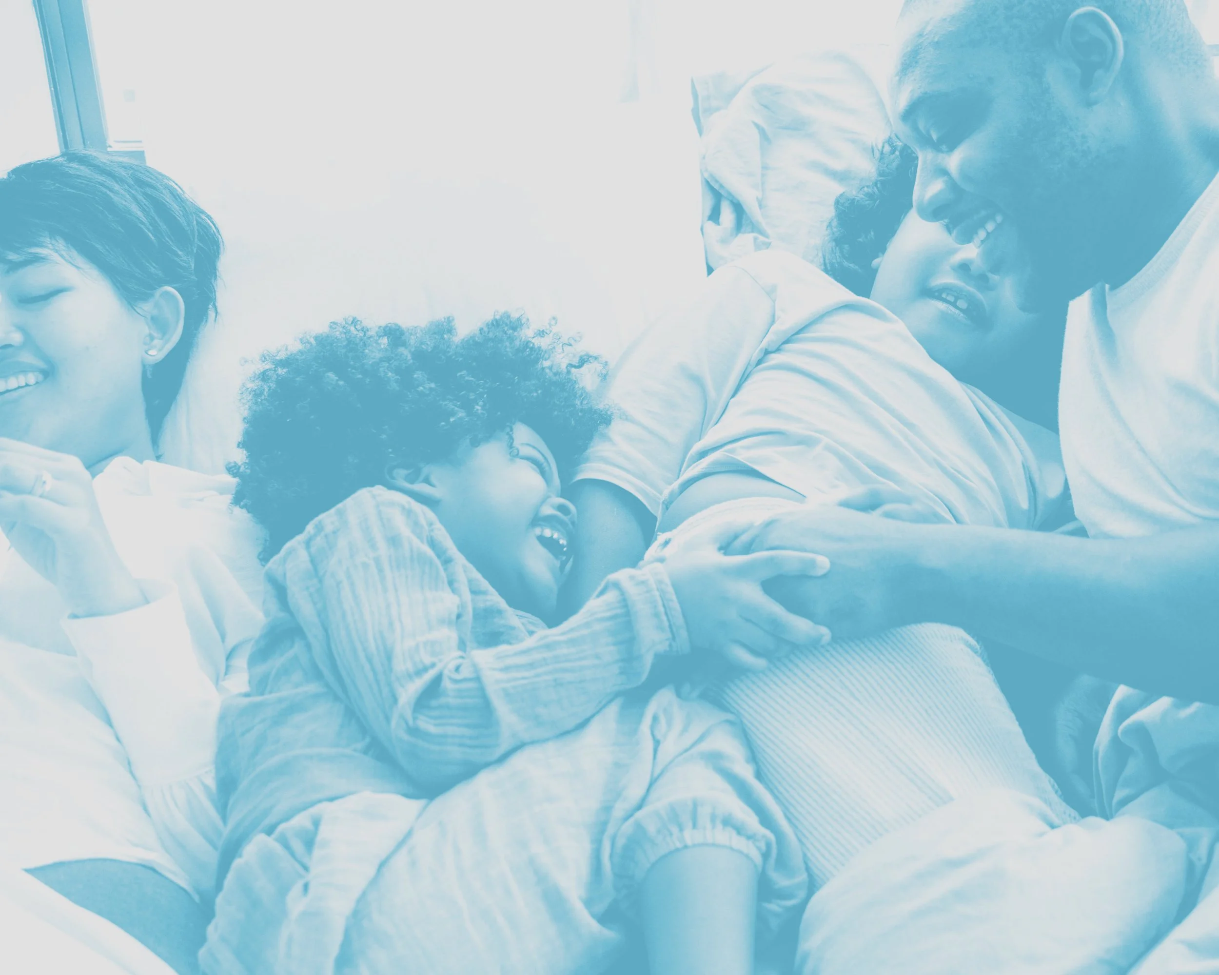A diverse group of four people lying in a hospital bed, smiling and laughing together, with one person in hospital gown and others in casual clothing, showing a moment of joy and connection.