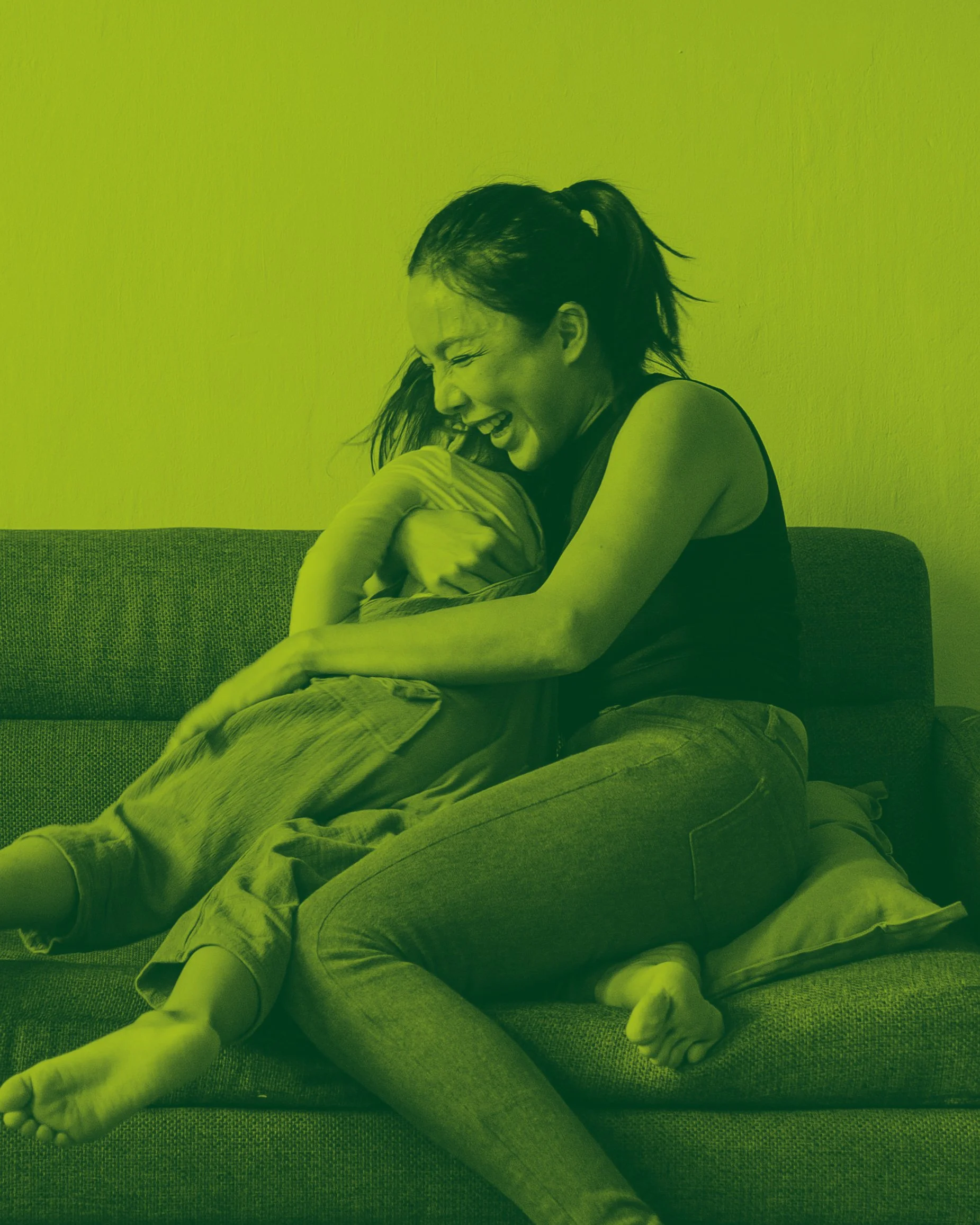 A woman and child sitting on a couch, hugging and laughing.