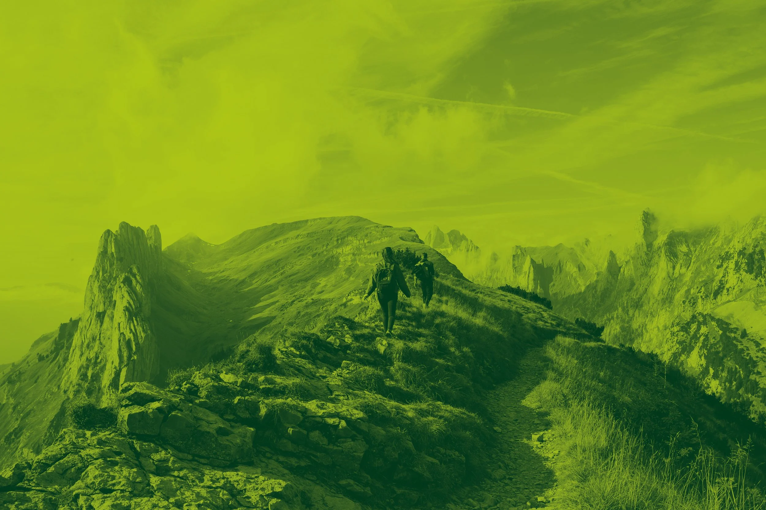 Hikers walking on a mountain trail with rugged peaks in the background.