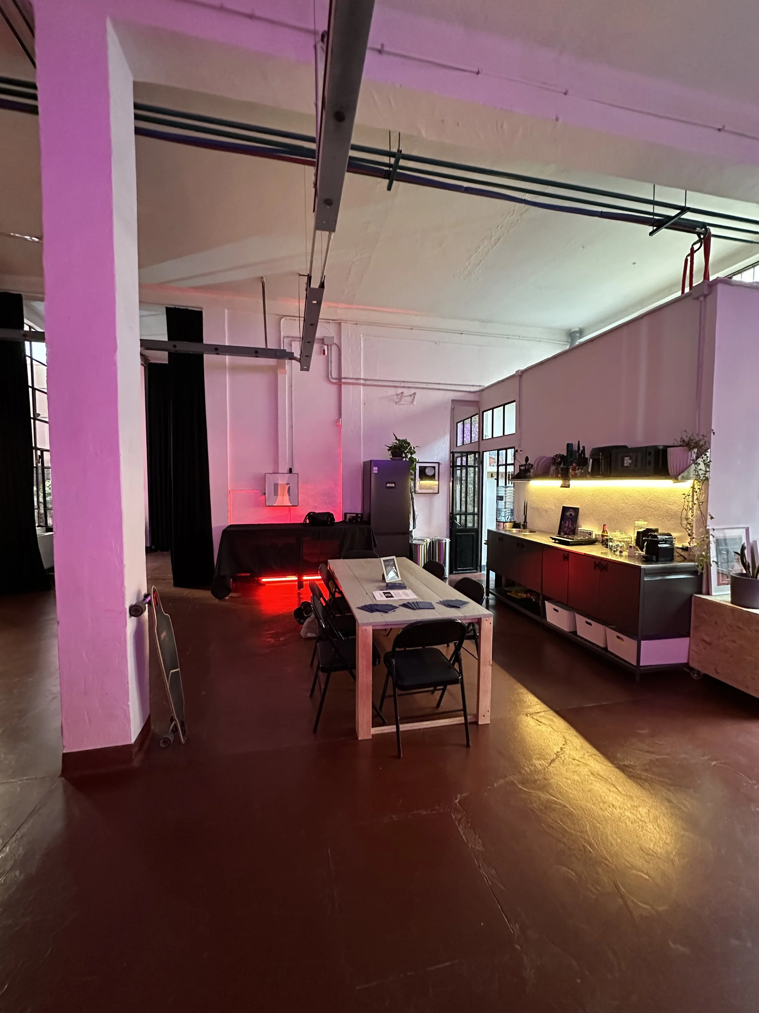 Interno di una stanza con tavolo, sedie, cucina e pannelli in stile industriale con tubi e luci calde.