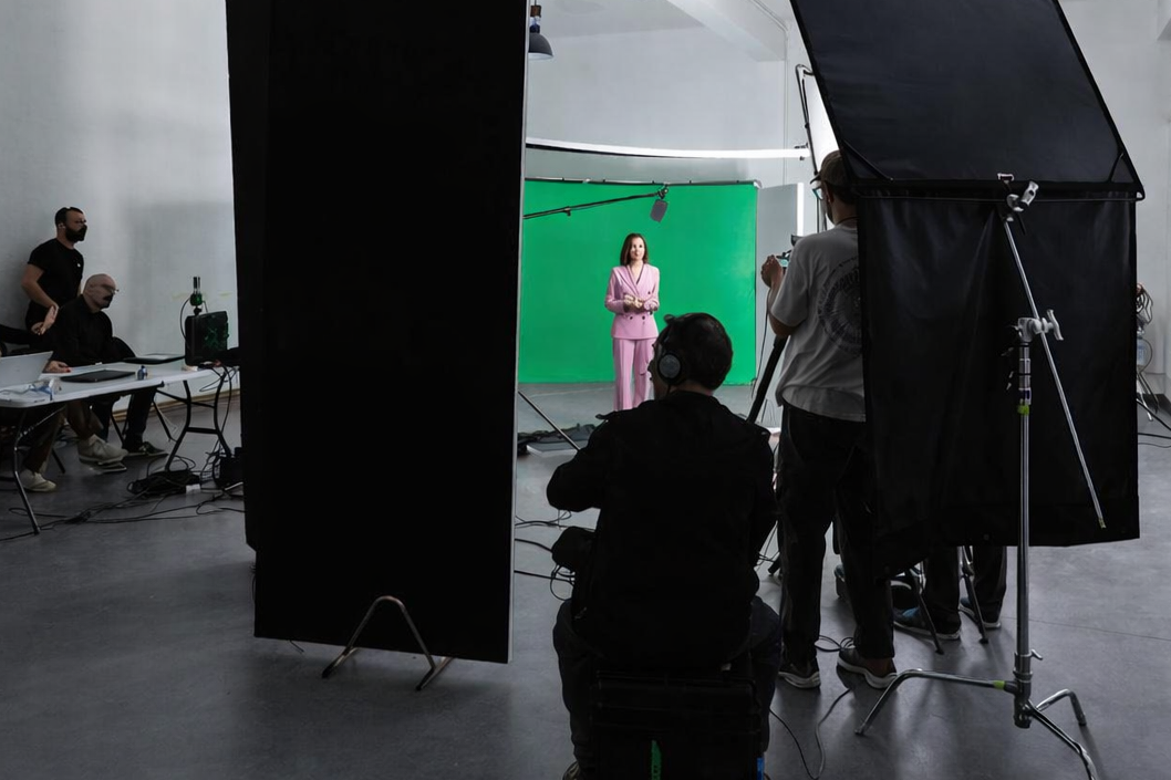Ripresa di una donna in abito rosa durante una registrazione in studio con sfondo verde e attrezzature di registrazione.
