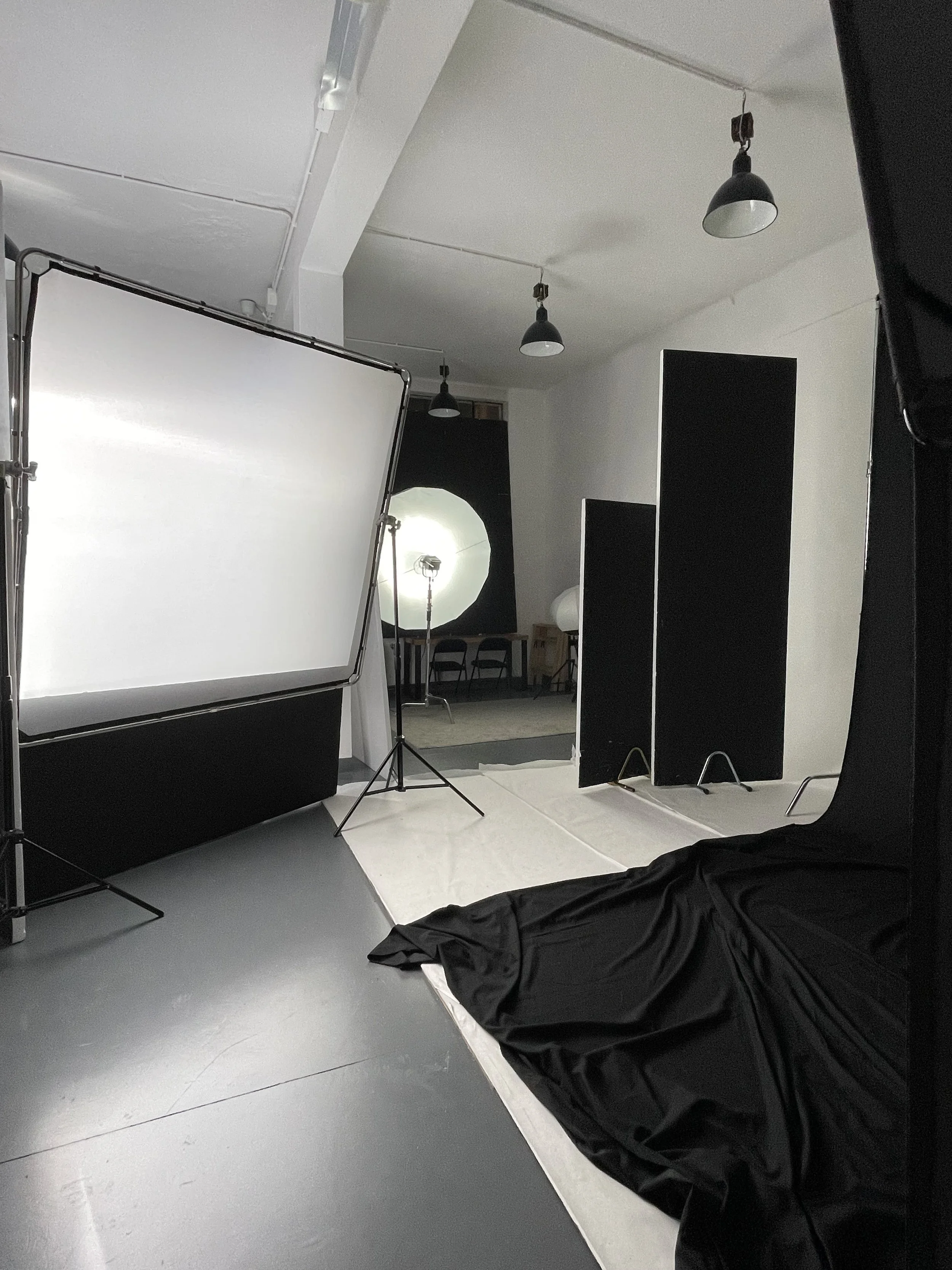 Set fotografico professionale in uno studio, con luci e pannelli neri, sfondo bianco, e attrezzature come schermate e luci.