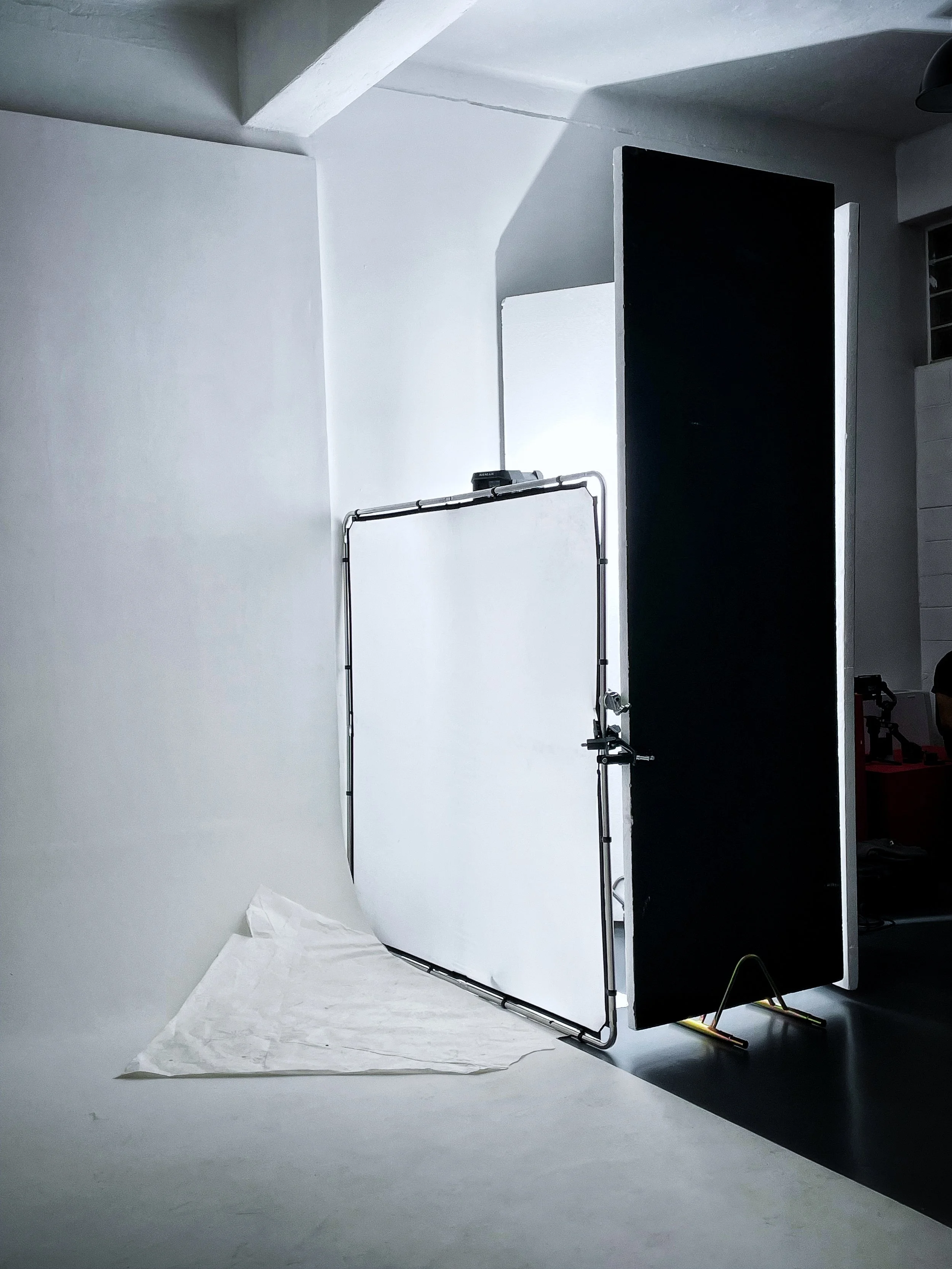 Foto di uno studio fotografico con schermo di sfondo bianco, una tenda nera e attrezzature fotografiche.
