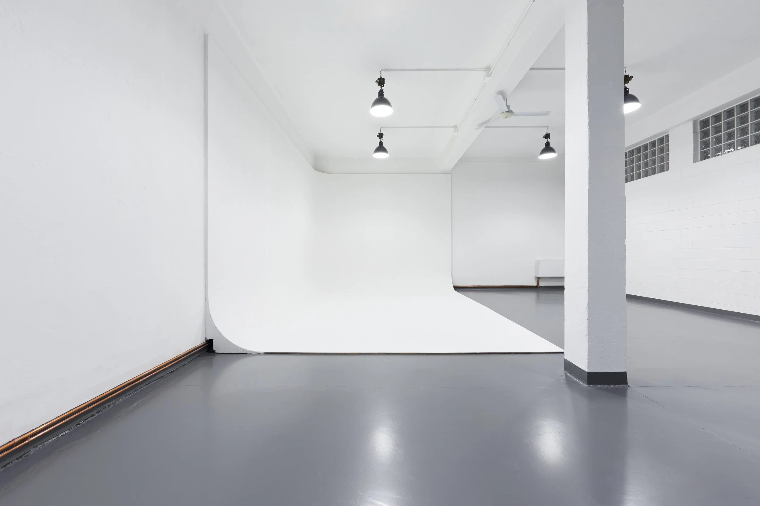 Uno studio fotografico vuoto con pareti bianche, pavimento grigio e luci sospese
