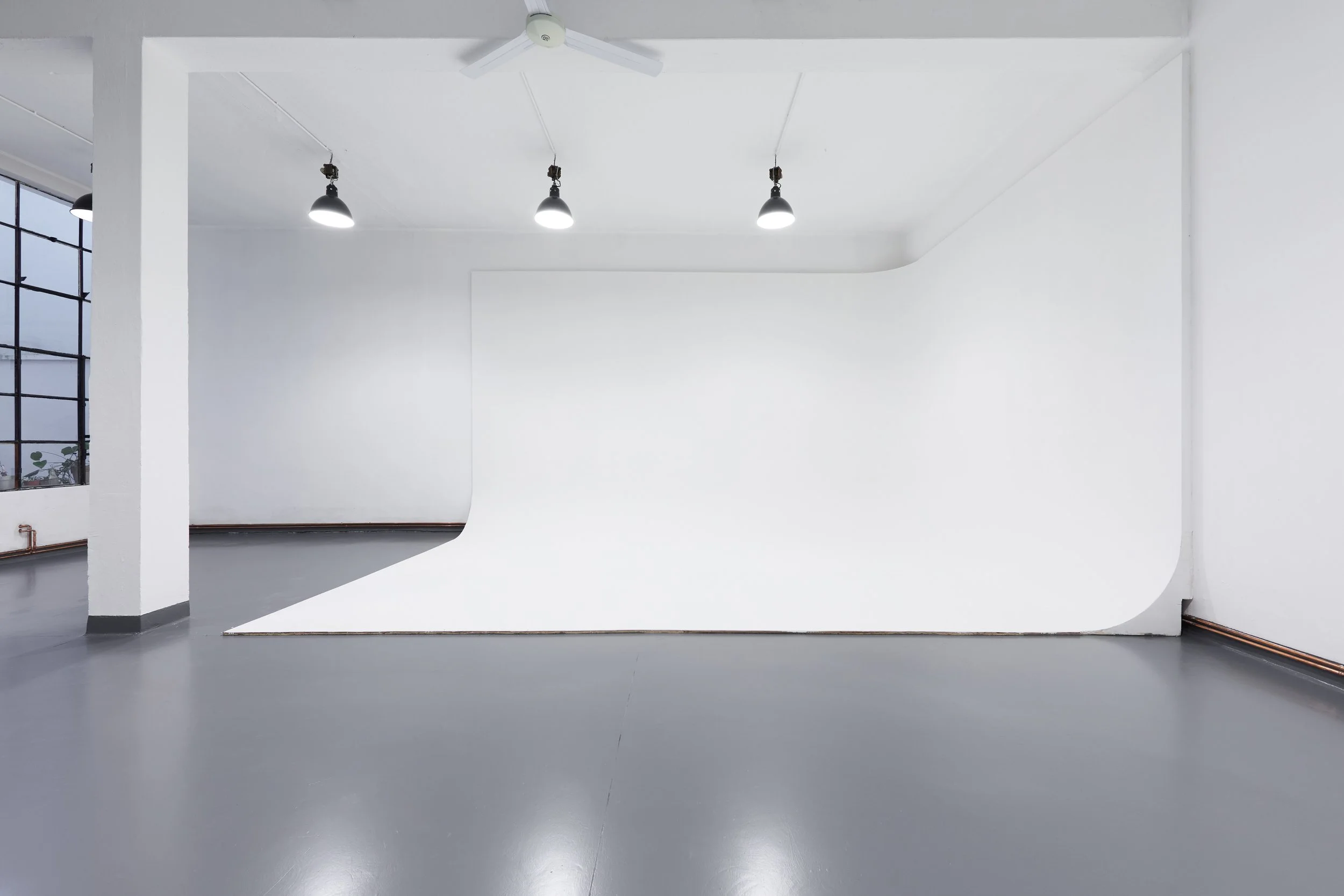 Studio fotografico vuoto con sfondo bianco mobile, luci a soffitto e grande finestra. Ciclorama ad L.