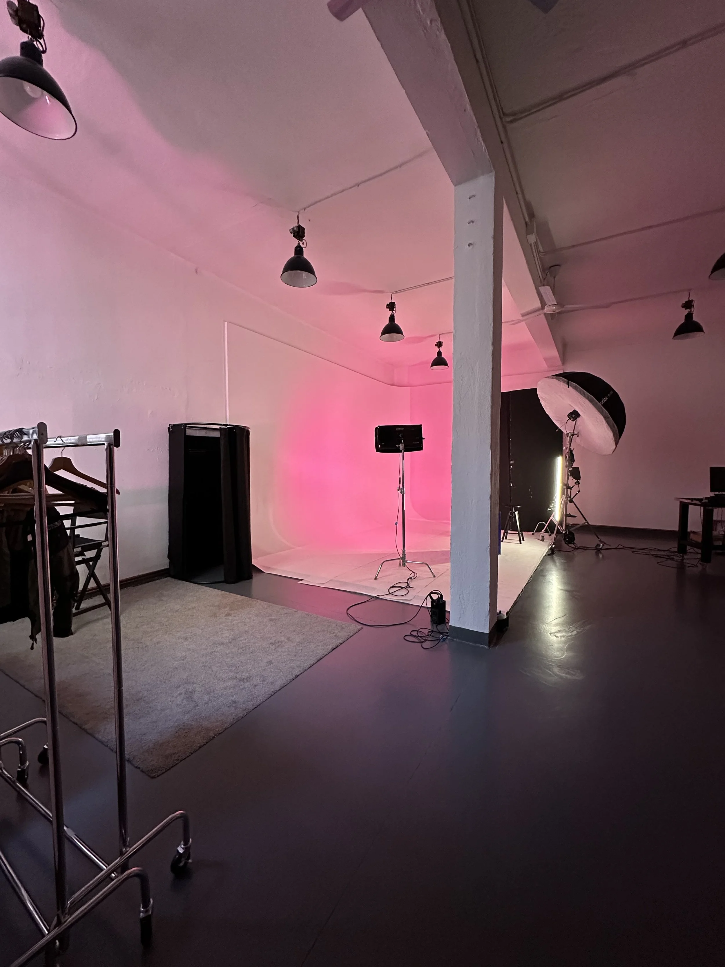 Interno di uno studio fotografico con fondale bianco illuminato da luci, attrezzatura fotografica e uno spazio vuoto pronto per un servizio fotografico.