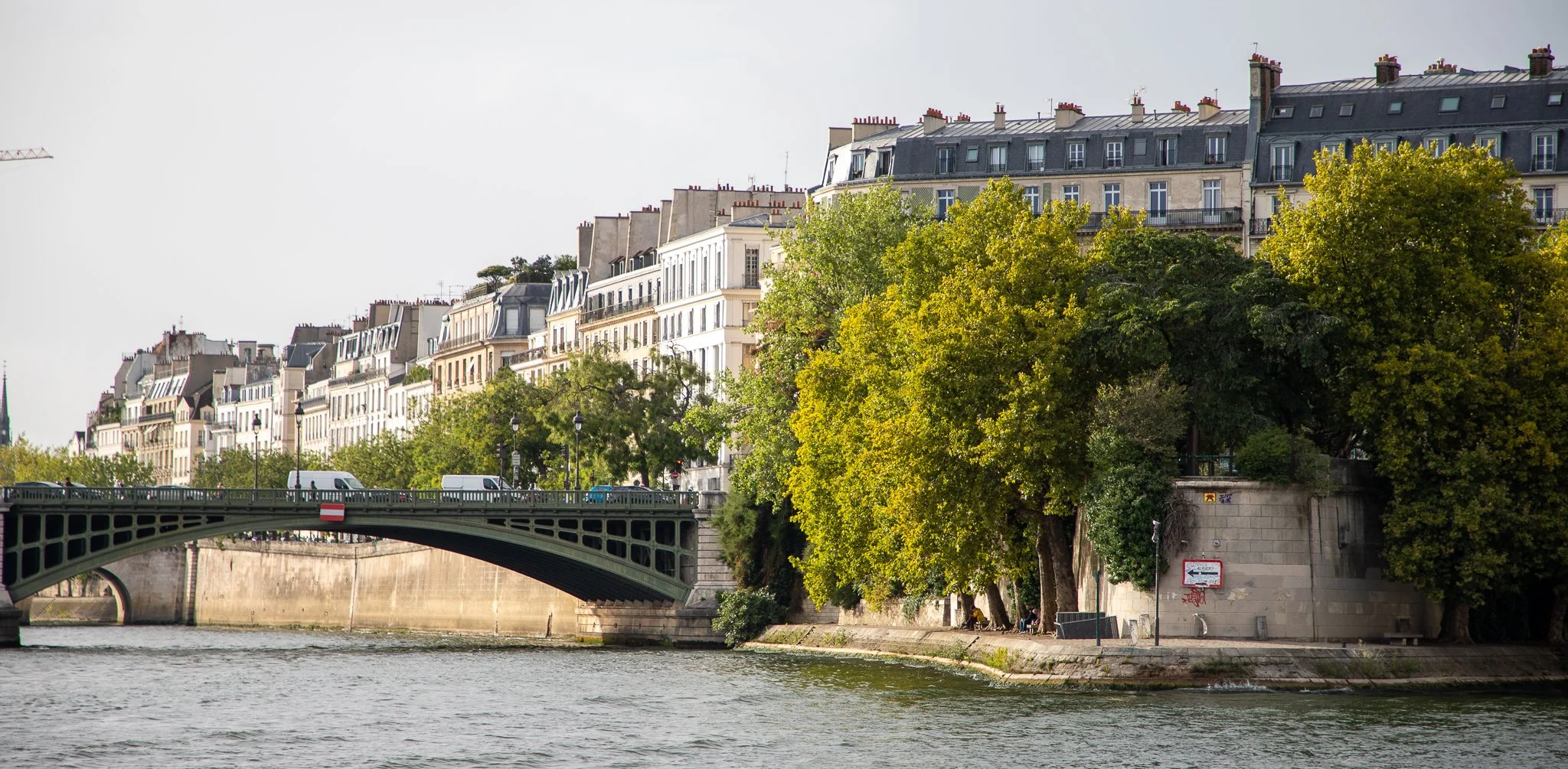 View of a bridge over a river with Parisian buildings and trees along the riverbank.