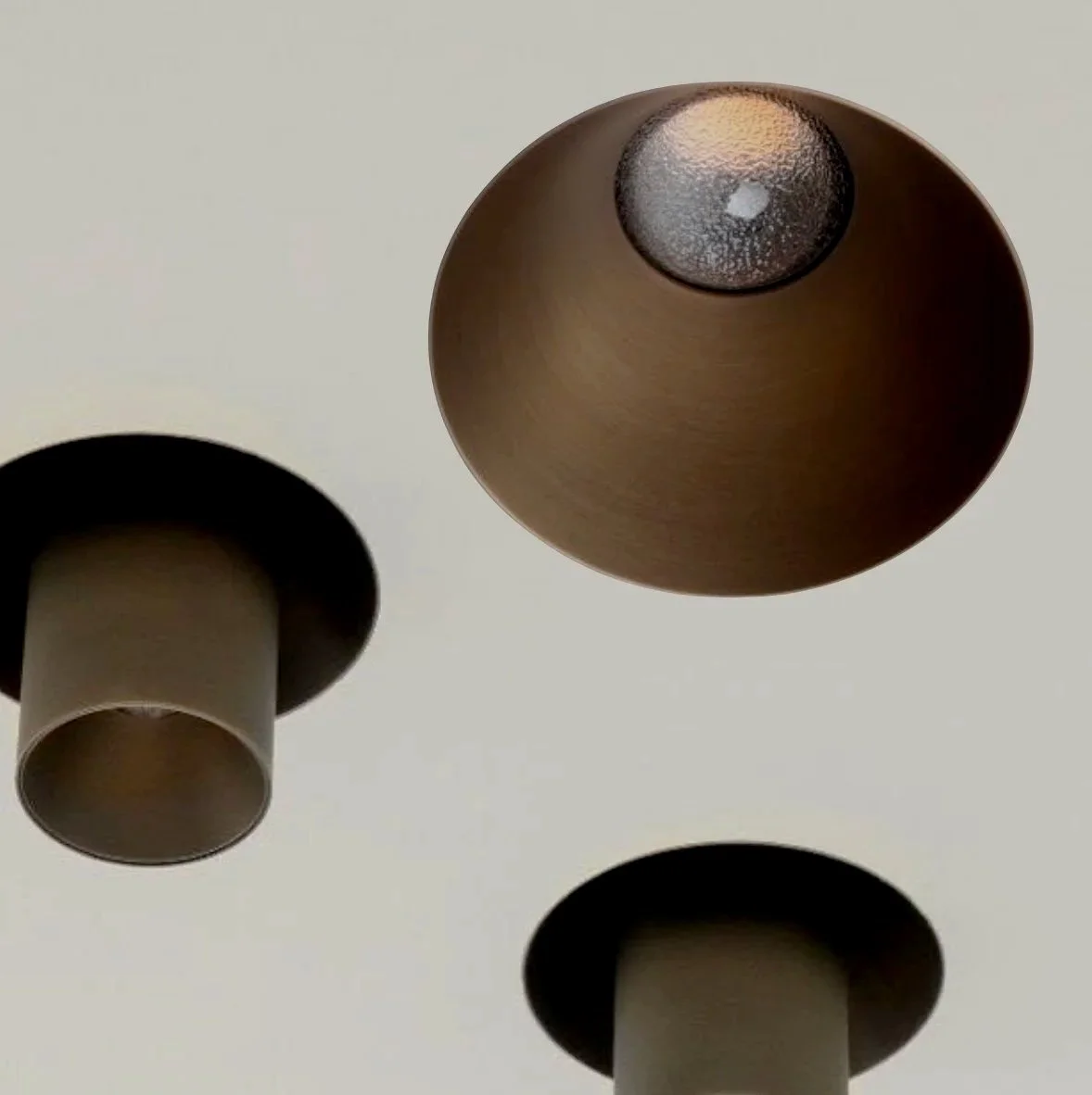 Billedet viser tre moderne loftslamper med cylindriske skærme, hvoraf en er brun og to er sorte, installeret på et lyst loft.