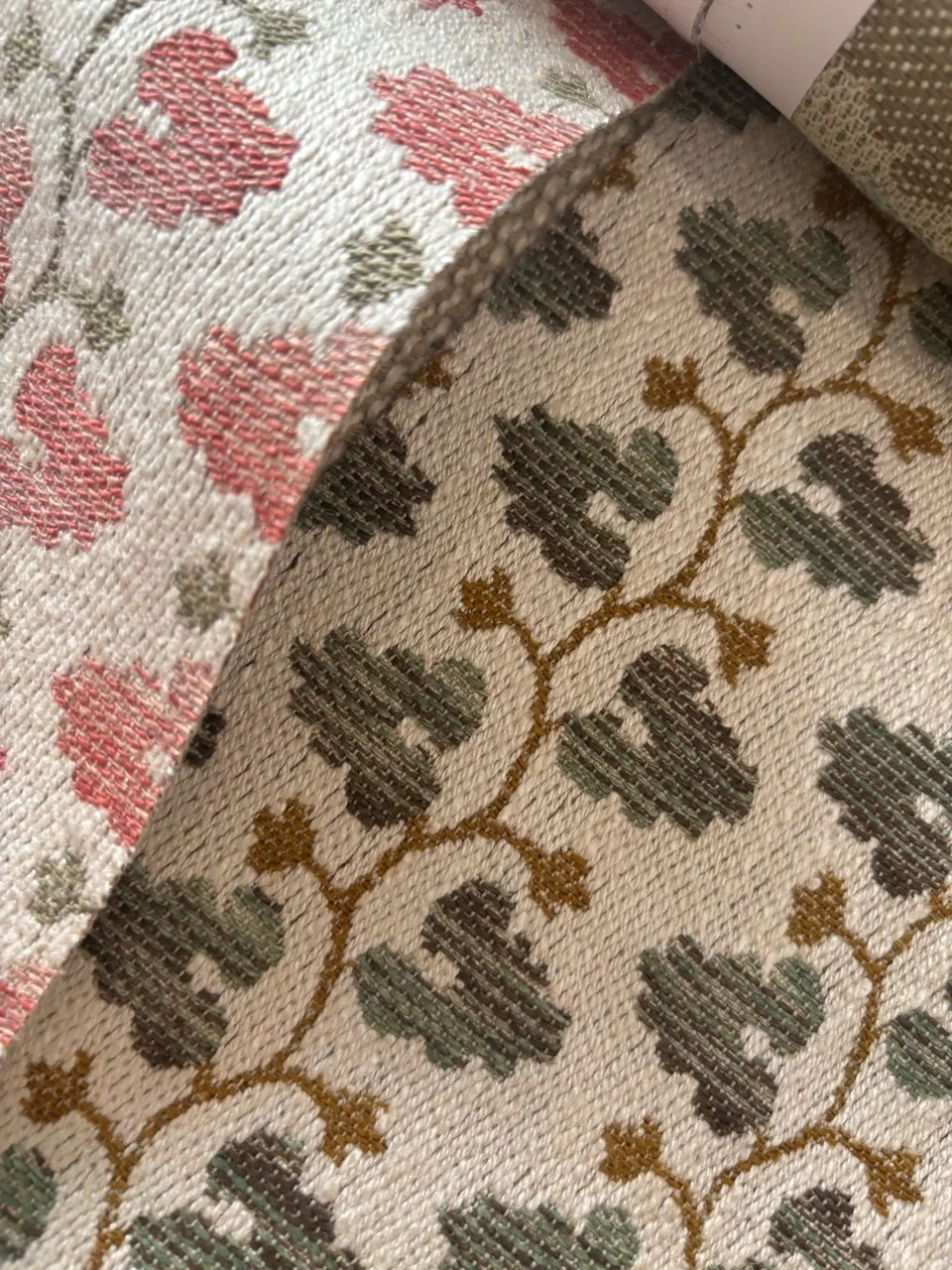 Tæppe med mønster af grønne blade og brune grene på en beige baggrund og et hørindpakket tekstilstykke.