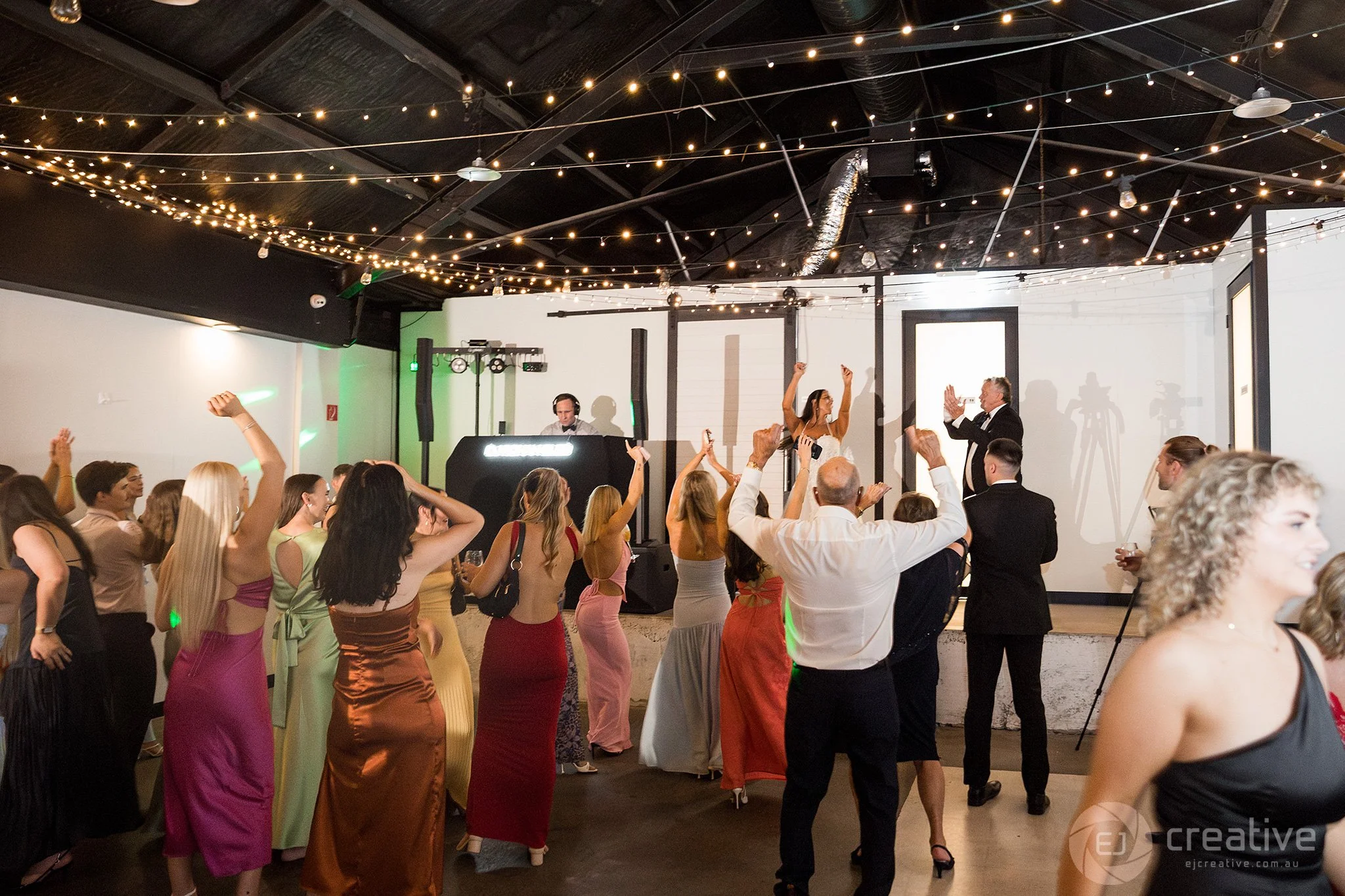 Photo of guests dancing at wedding with DJ Rohan Blee in the background behind his black DJ booth.