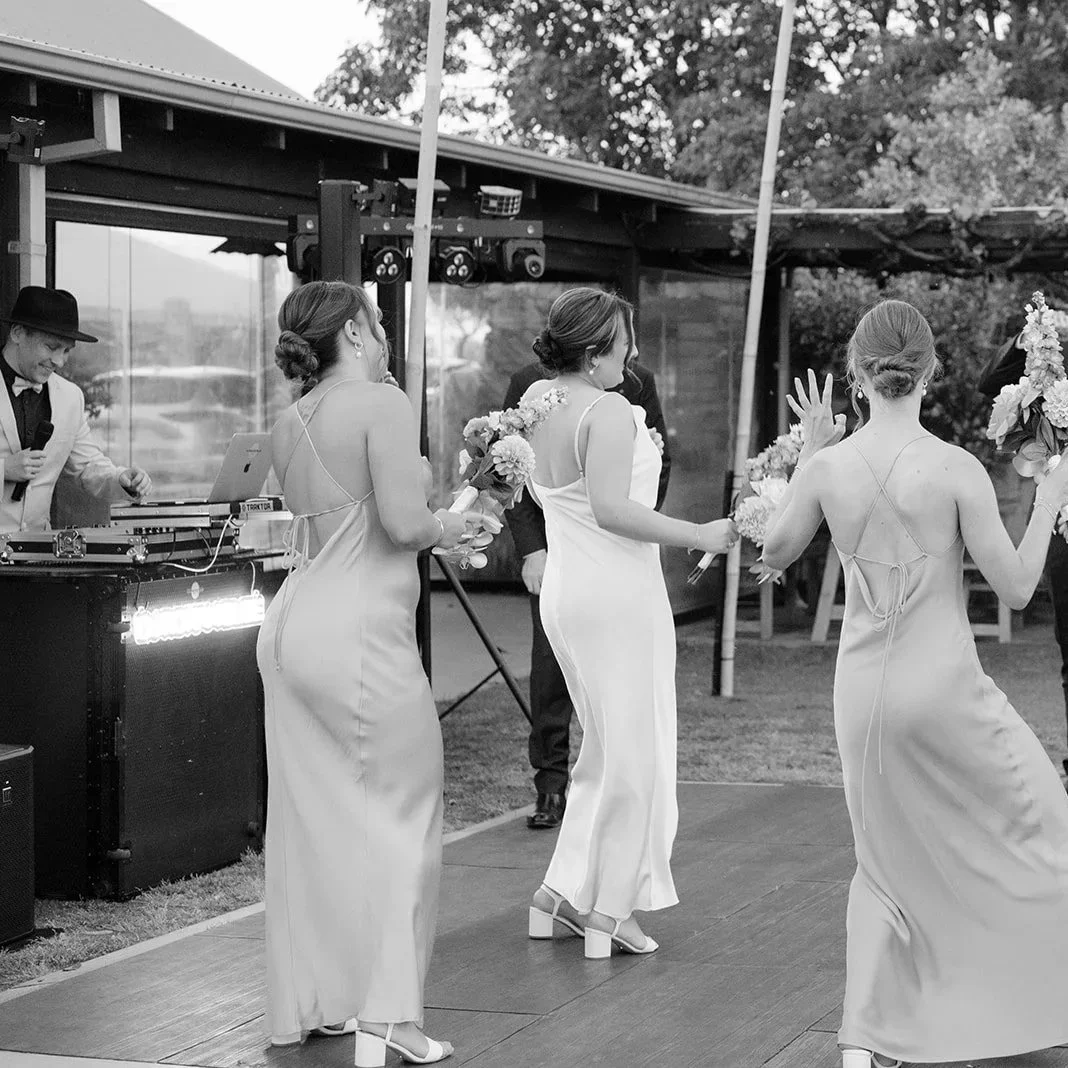 Black and white photo of bridesmaids and bride dancing in front of DJ Rohan Blee's booth.