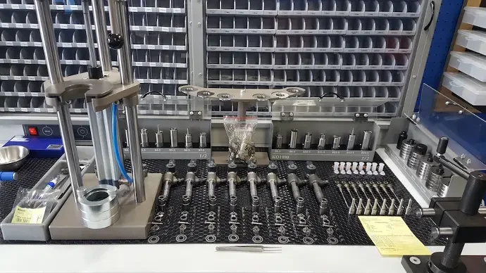 Laboratory workbench with precision tools, q-tips, metal parts, and a plastic bag containing small objects.