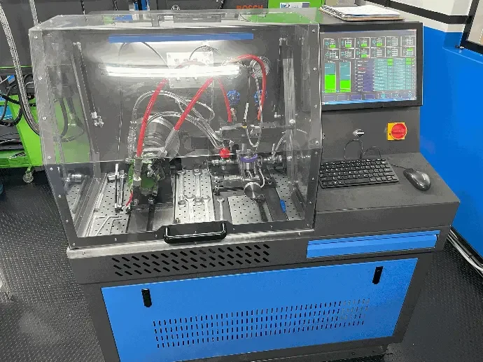 A desktop industrial machine enclosed in a clear plastic cover with red and black tubes inside, a control panel with a computer monitor, keyboard, and mouse.