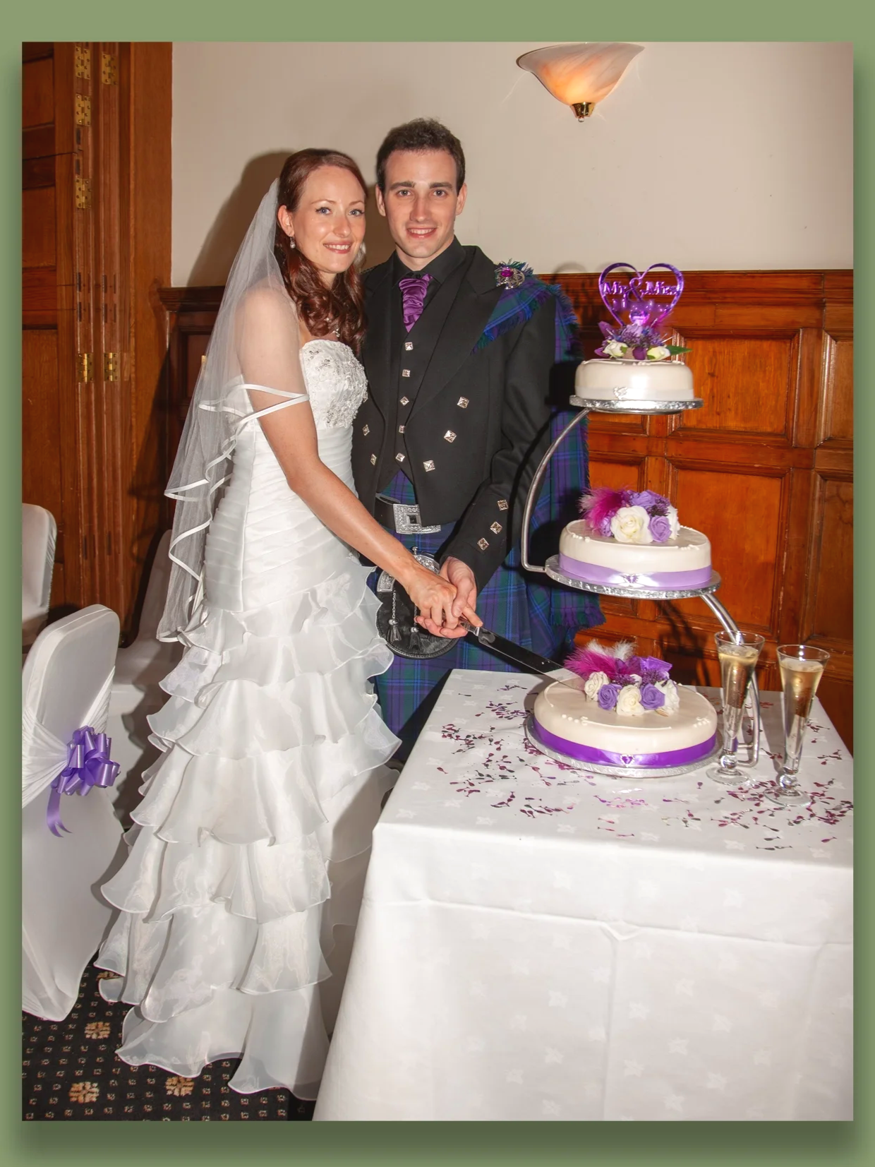 Bride and groom cutting a wedding cake at their reception, with purple and white decorations.