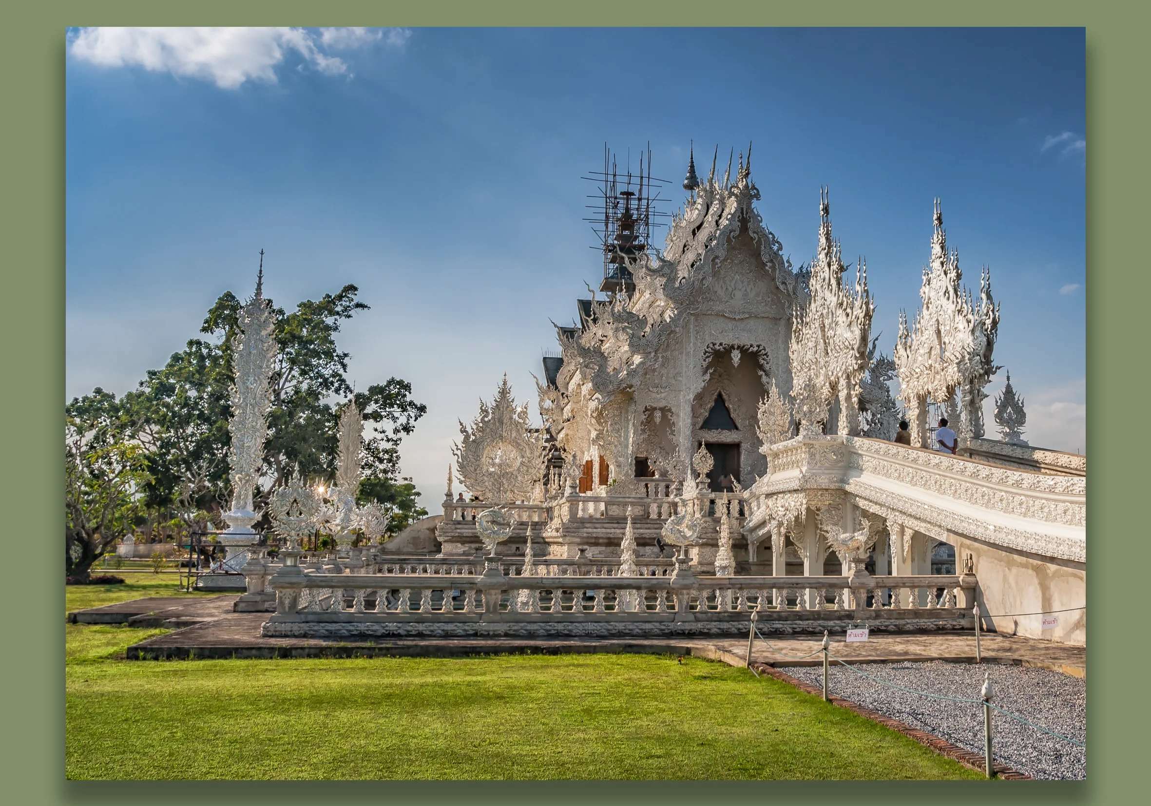 Chiang Mai. White ornate temple with elaborate carvings and spires, surrounded by a garden and a stone pathway under a blue sky.