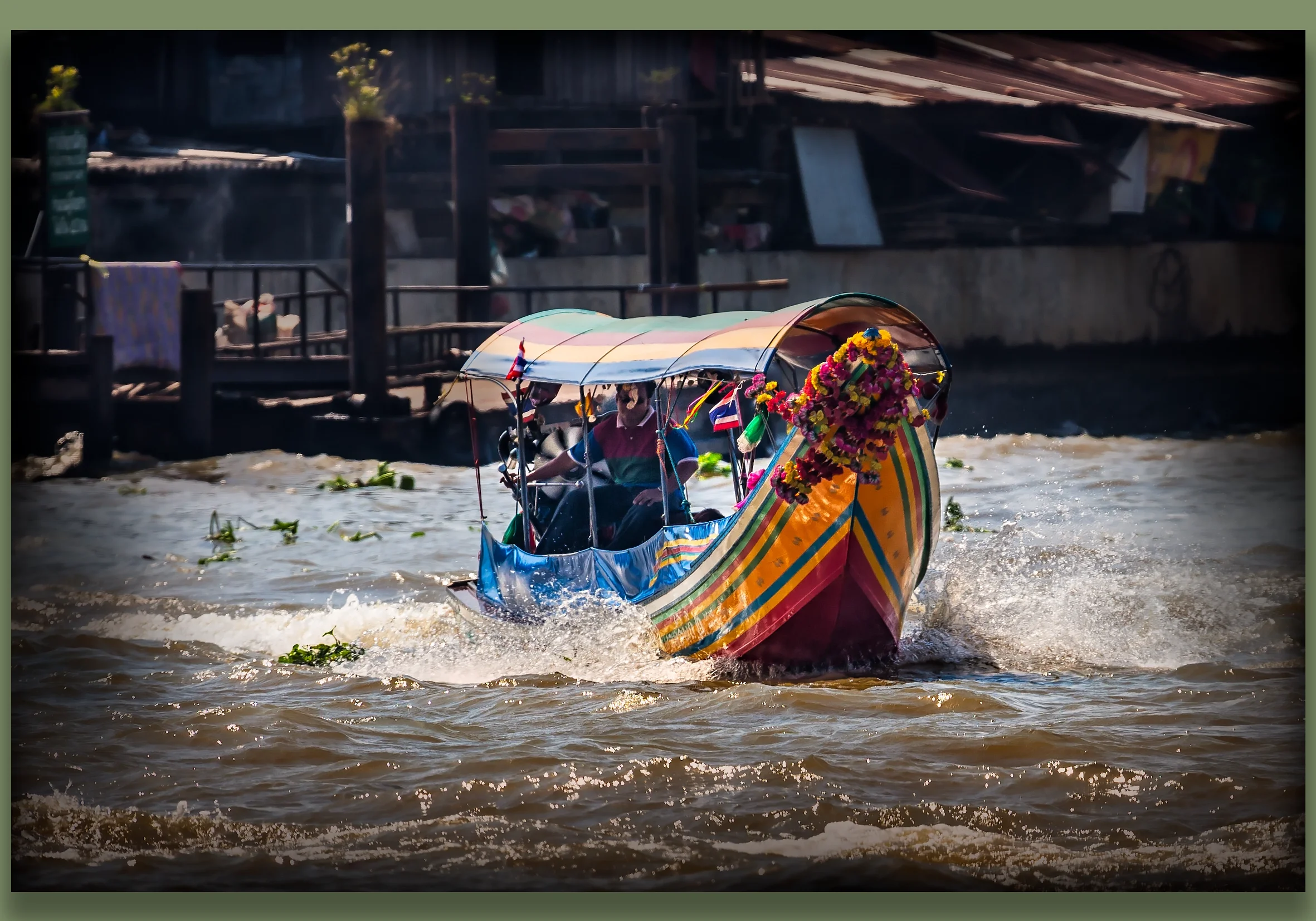 Colourful traditional boat decorated with flowers and flags, sailing on a canal in Bangkok.
