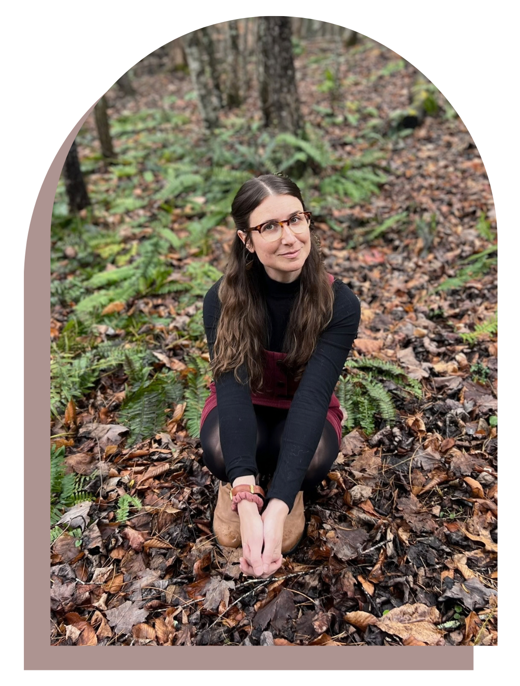 Meredith Rosenbluth kneeling on a forest floor covered with fallen leaves, with green plants and trees in the background.