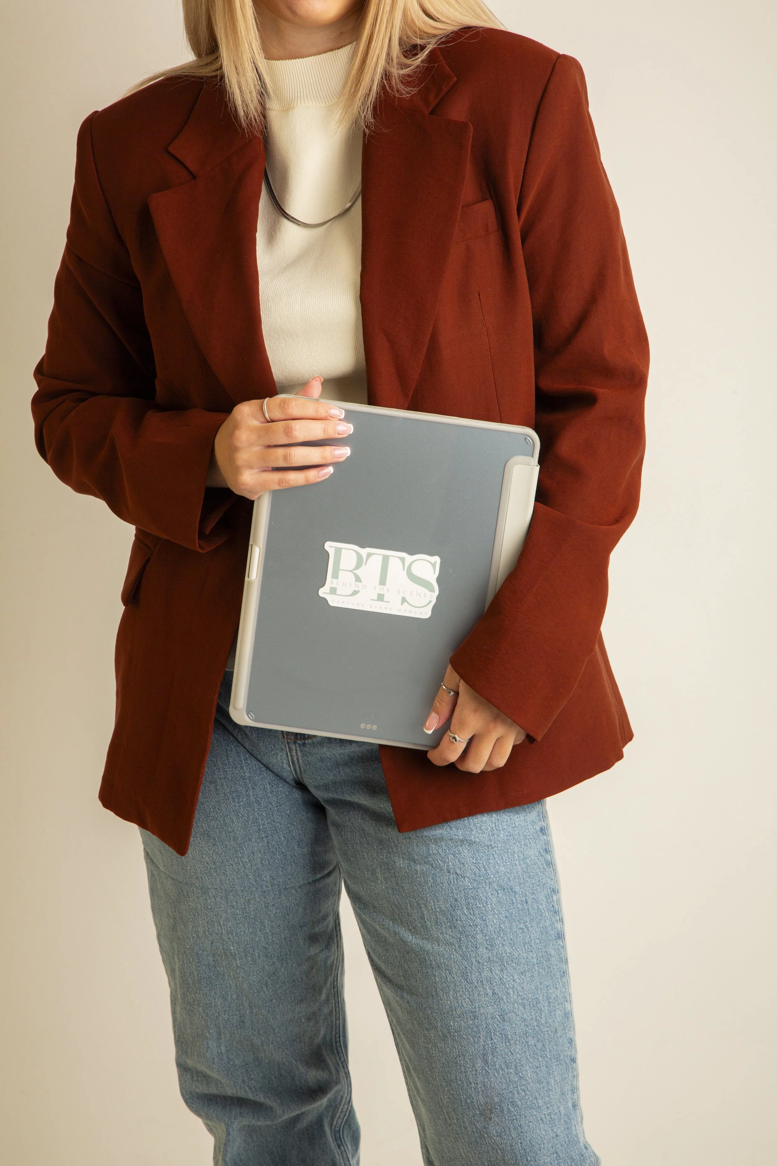 Person wearing a brown blazer and jeans holding a laptop with the BTS logo on it.