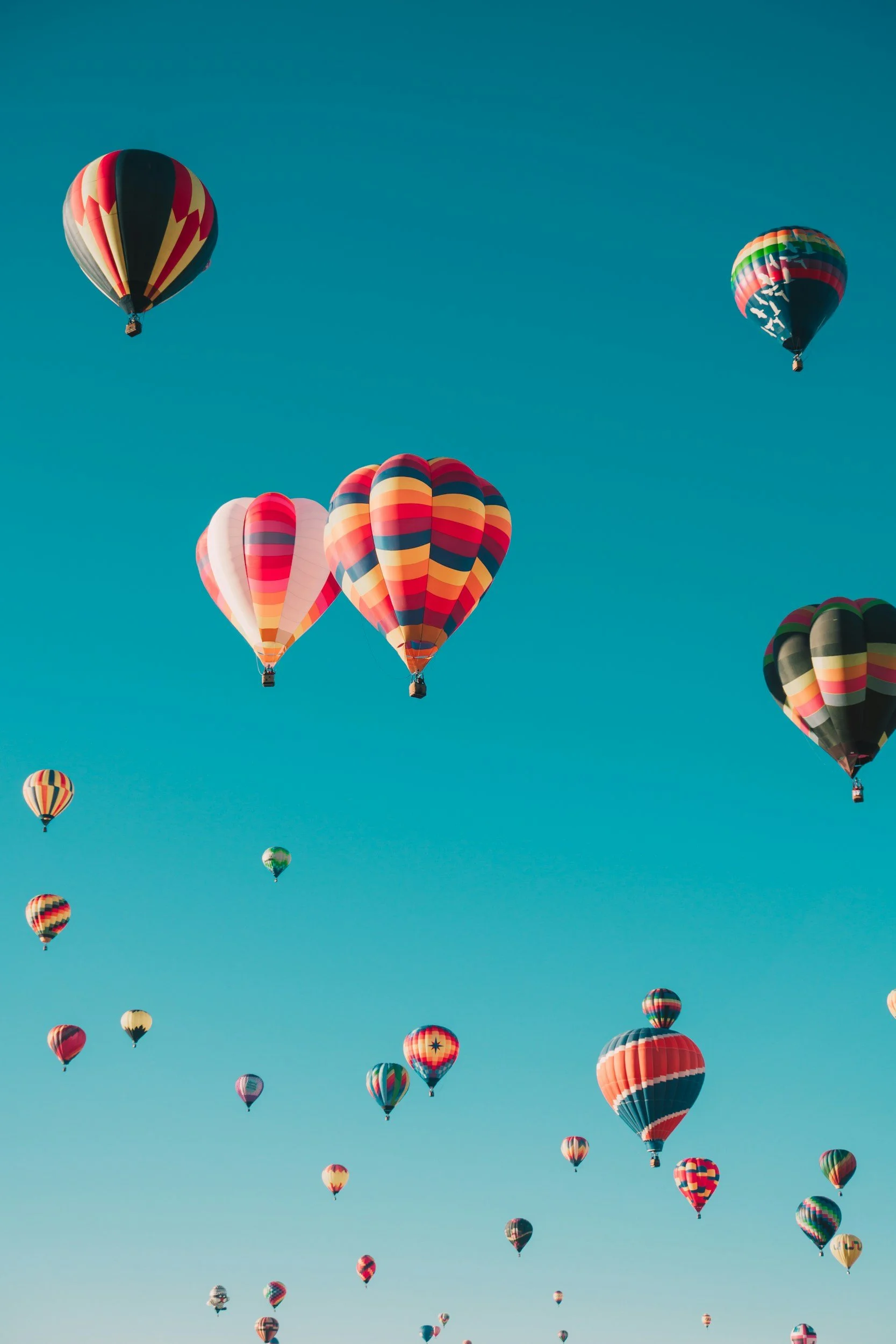 Multiple colorful hot air balloons flying in a clear blue sky.