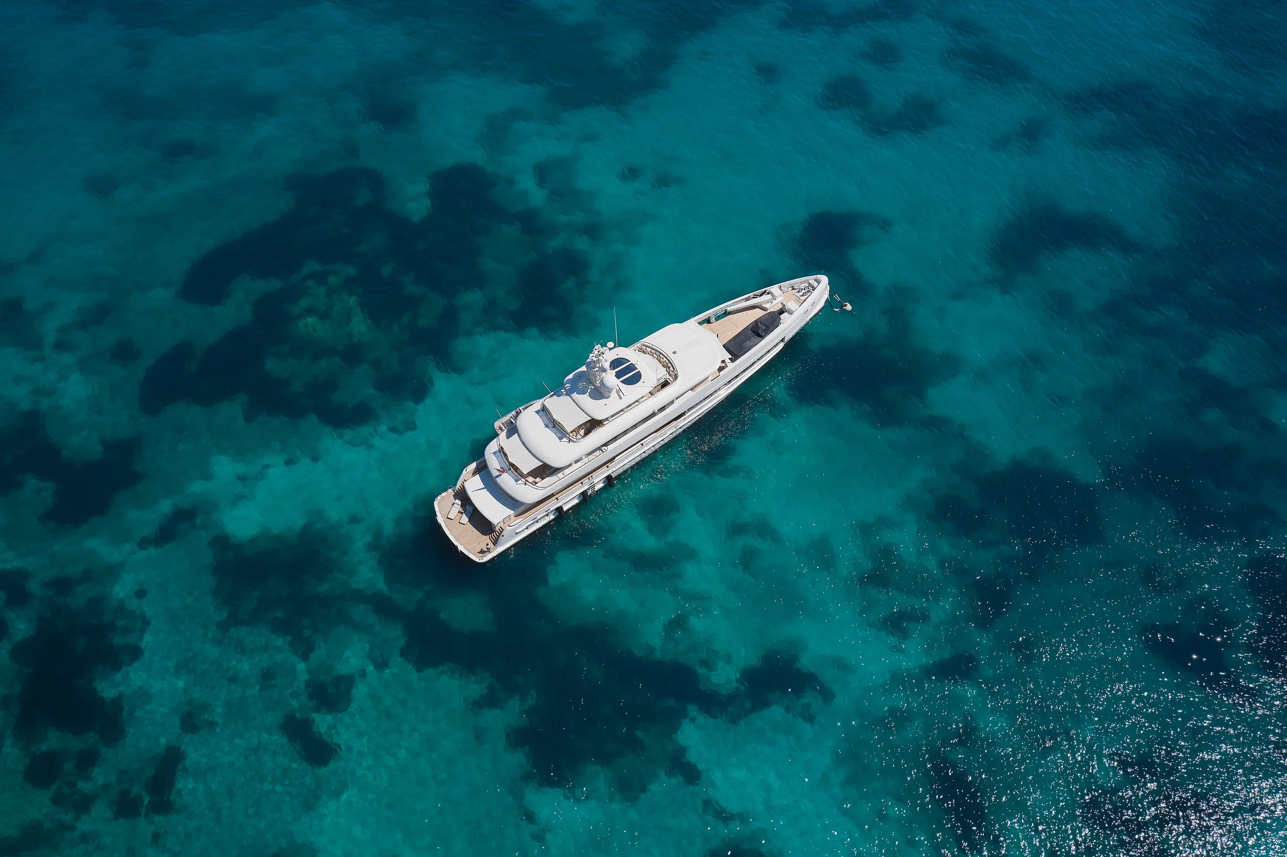 Overhead view of a large white yacht sailing in clear turquoise water with visible coral reefs beneath