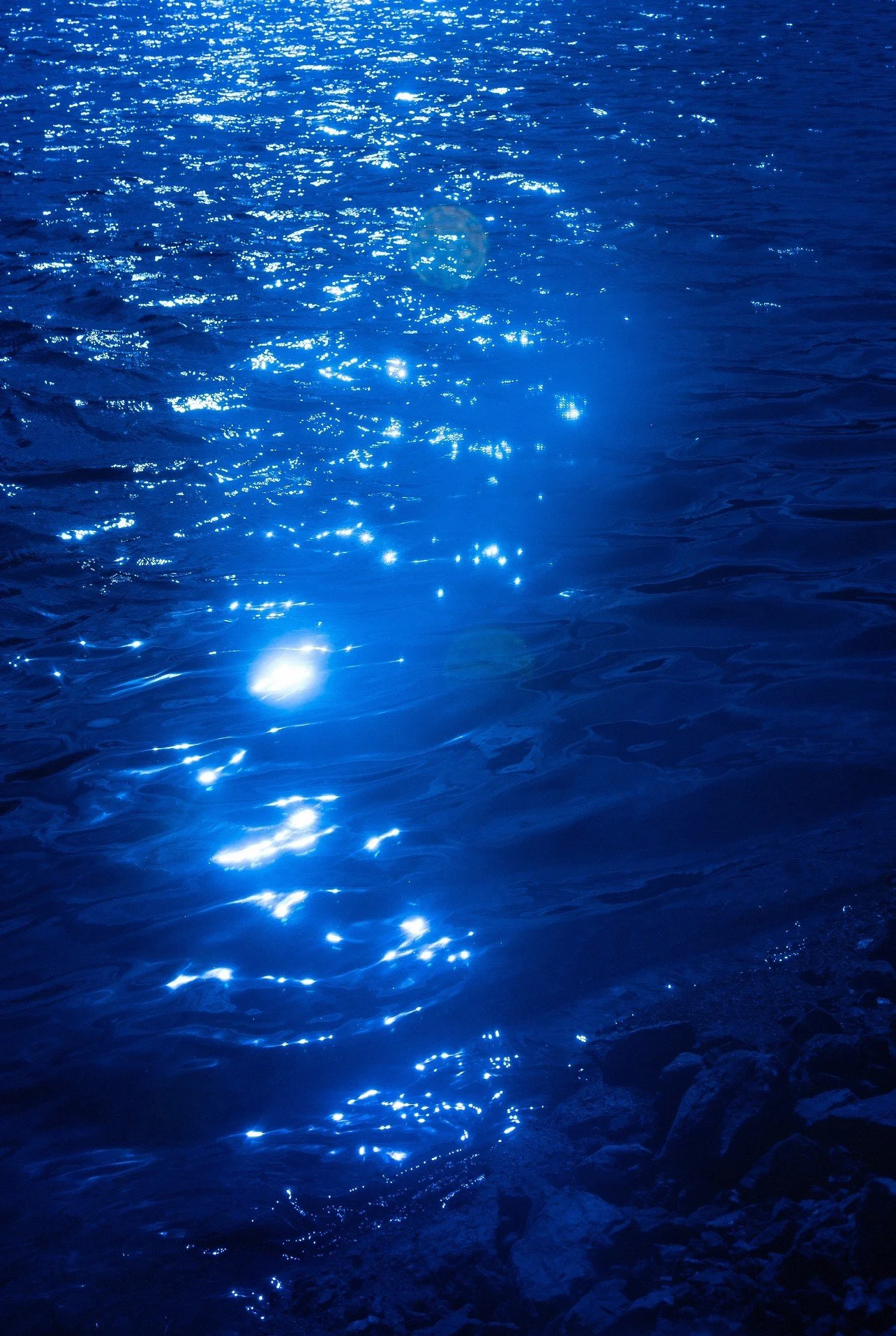 Sunlight reflecting on a body of water, creating bright, sparkling spots on the blue surface.