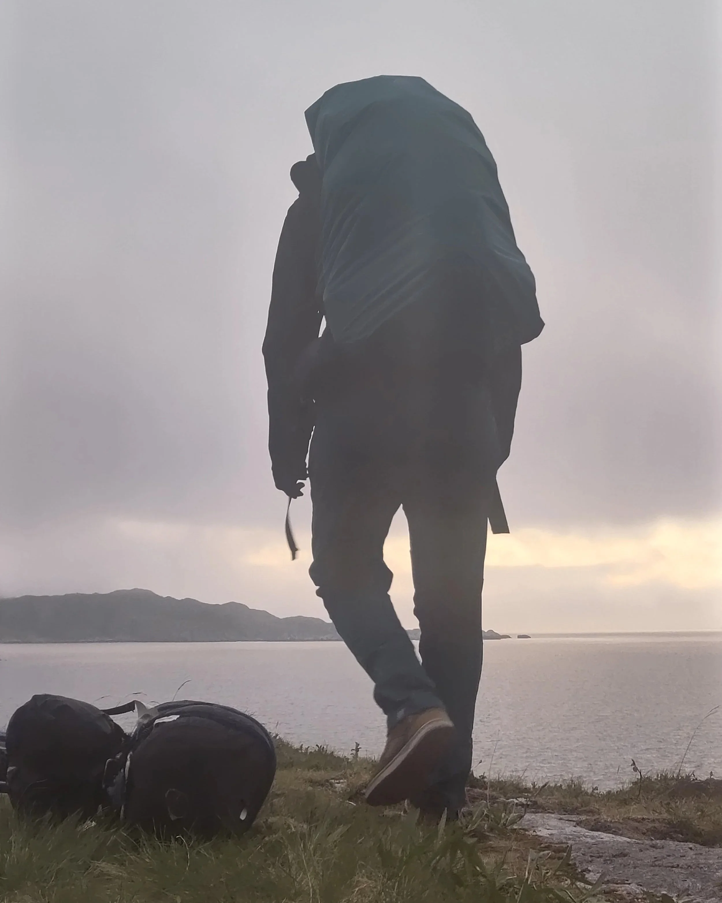Une silhouette d'une personne avec un sac à dos, près d'un lac ou d'une mer, sous un ciel nuageux.