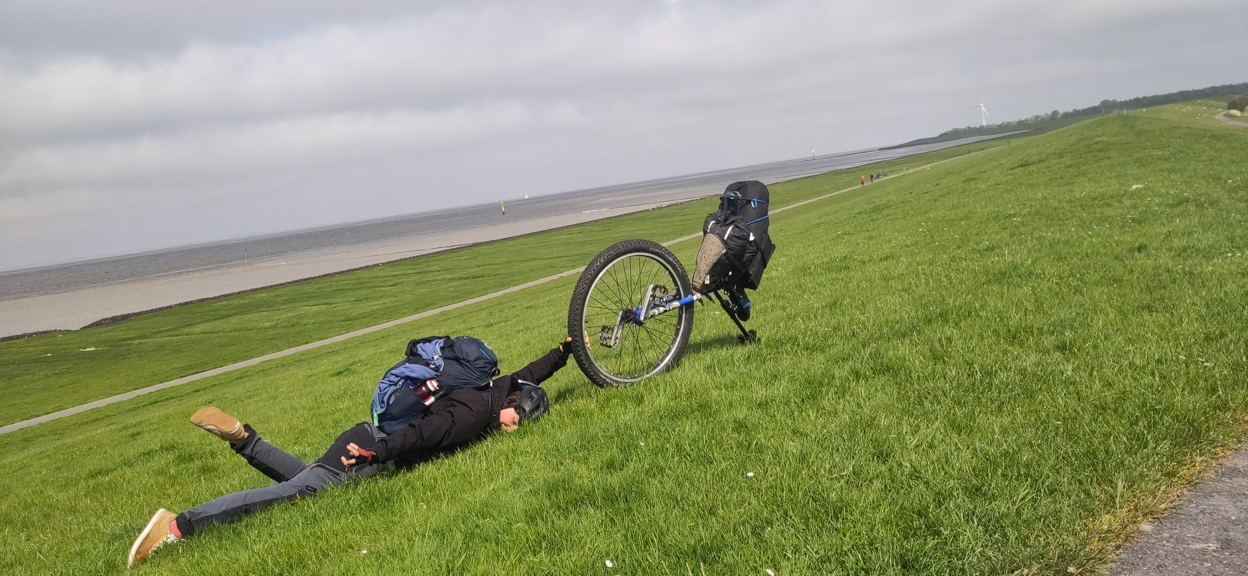 Monocycliste se faisant trainer par son monocycle dans l'herbe dans un paysage en plein air avec un ciel nuageux et un terrain en pente.