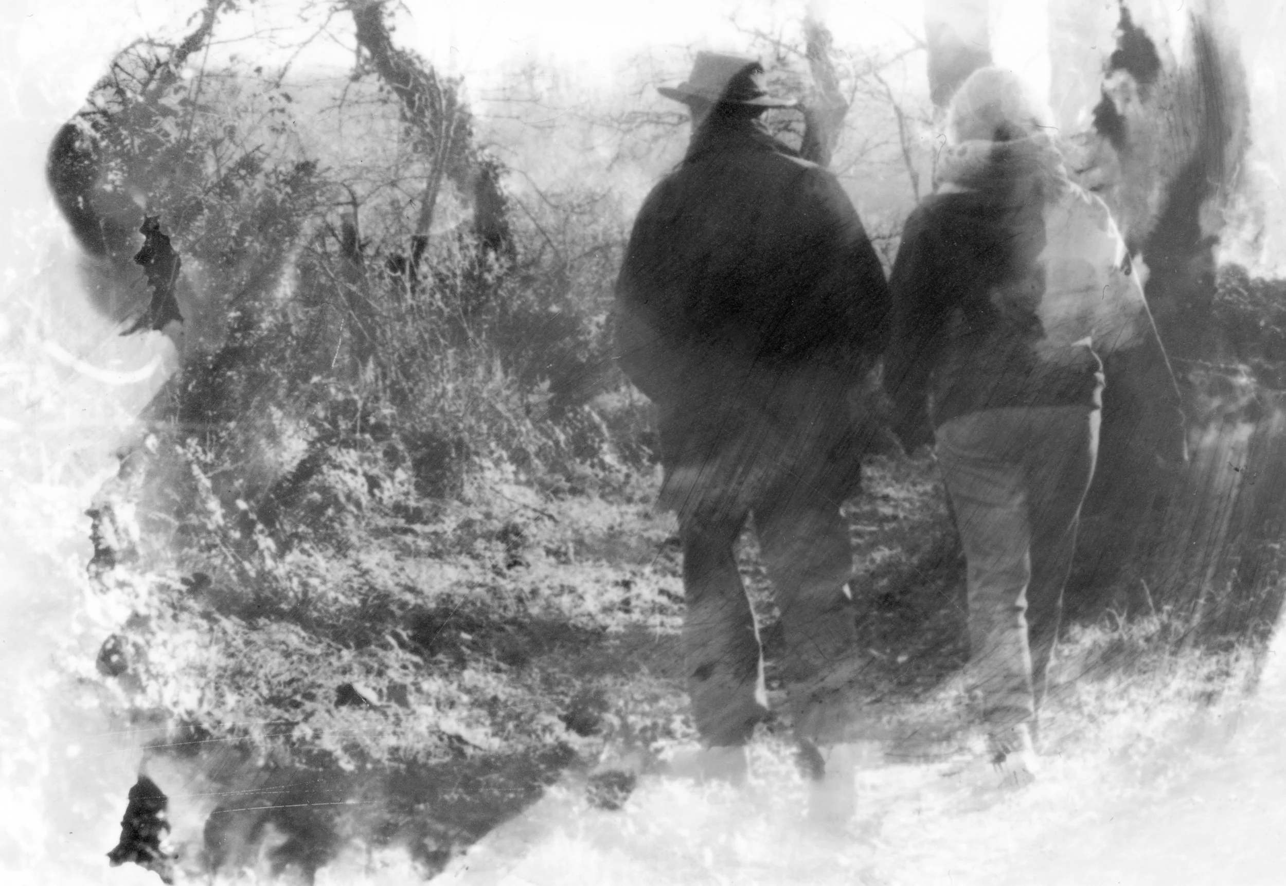 Trois personnes marchant dans un paysage naturel avec des arbres, deux d'entre elles portent un costume sombre et un chapeau, la troisième porte un vêtement clair. L'image est en noir et blanc avec un effet flou et superposé.