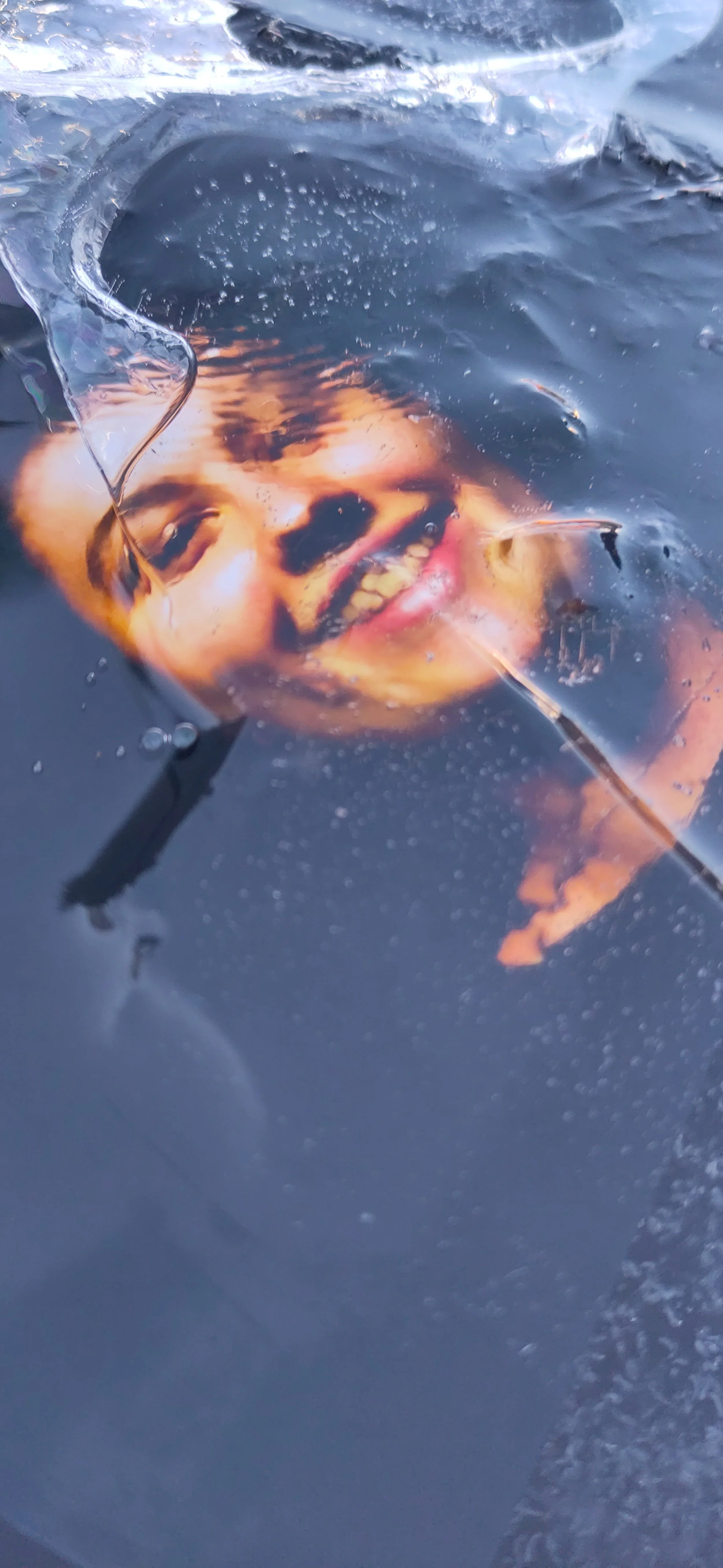 Photo d'une personne souriante en train de nager sous l'eau, avec de l'eau claire autour, semblant faire une plongée ou nager en surface.