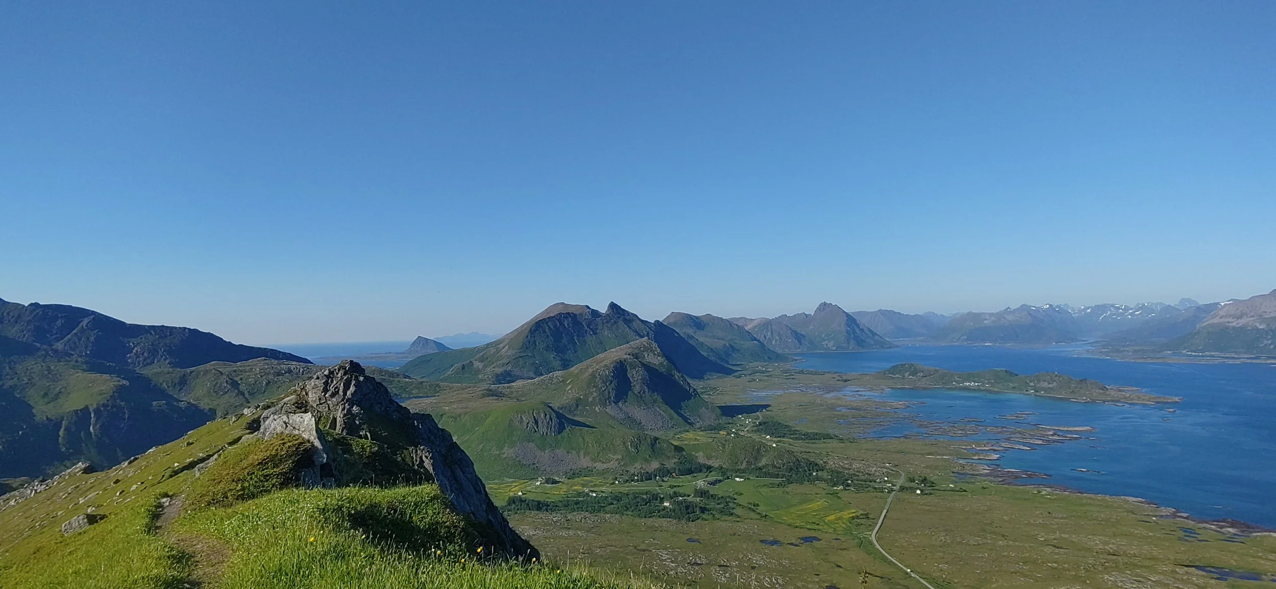 Paysage de montagnes verdoyantes avec des lacs au bord de la mer sous un ciel clair.