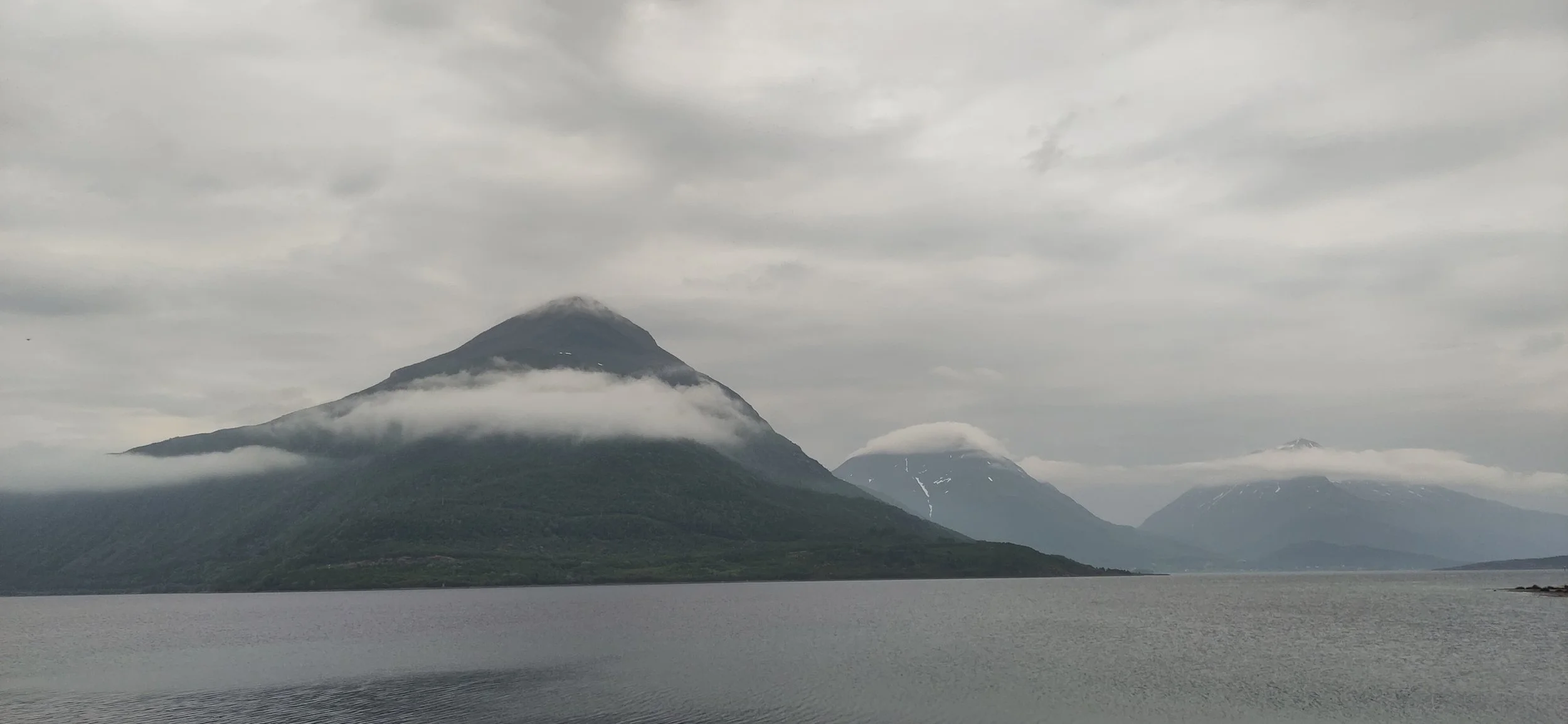 Paysage de montagnes avec des sommets enneigés, entourées de nuages, vue sur un plan d'eau calme