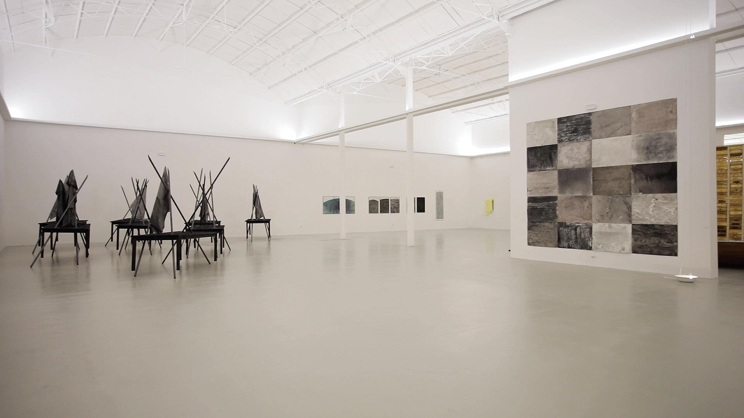 Galerieraum mit Kunstwerken, darunter Skulpturen aus verbrannten Tischen und große Wandbilder, alles in einem modernen Kunstmuseum, Teil der Ausstellung im Museum Camusac in Cassino vom zeitgenössischem Düsseldorfer  Künstler Eduard Winklhofer