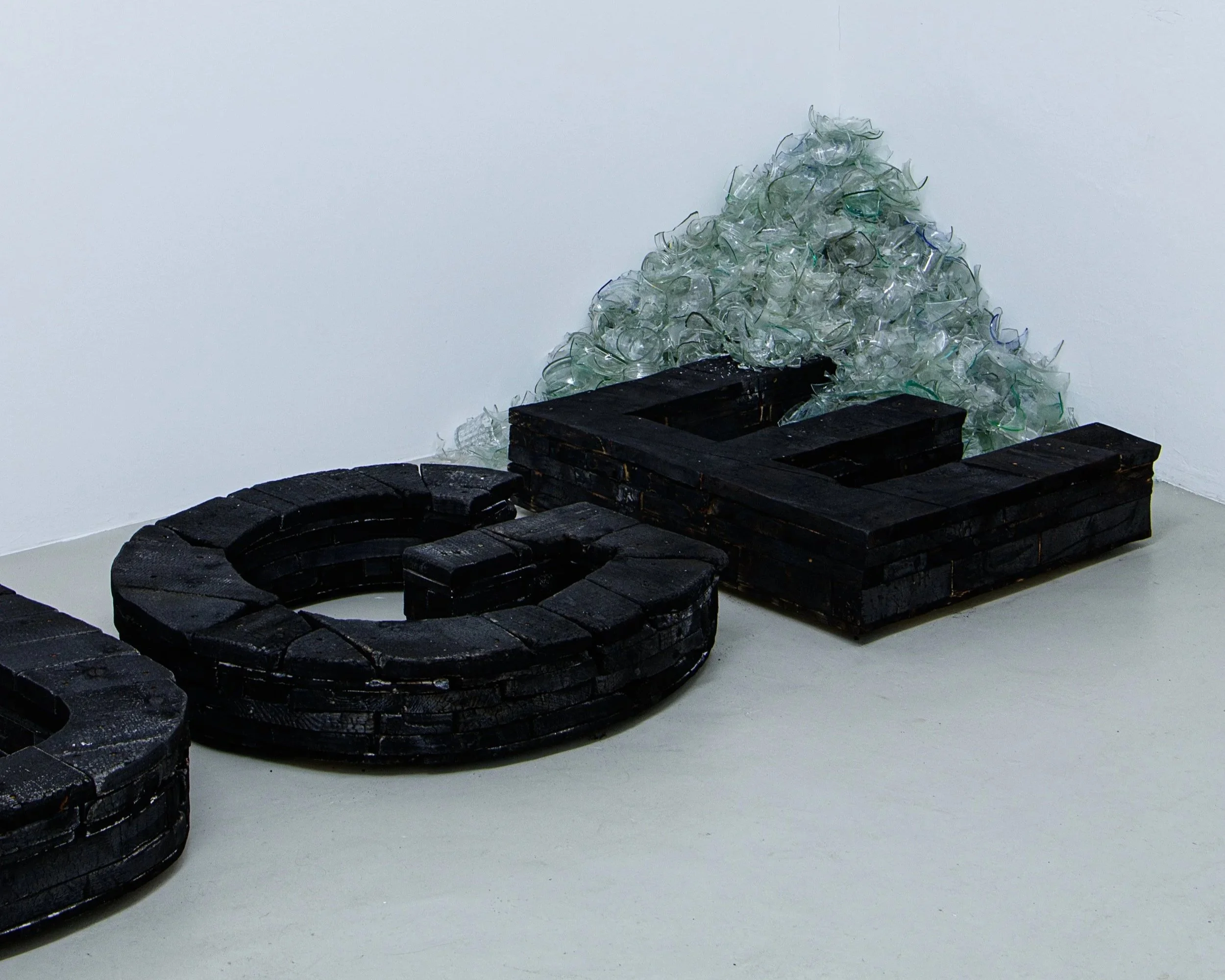 Kunstinstallation mit schwarzen Holzbuchstaben und einer Pyramide aus Glasscherben, Auge, verbranntes Holz, Glasscherben, Raum für Kunst Oberkassel des zeitgenössischen deutschen Künstlers Eduard Winklhofer