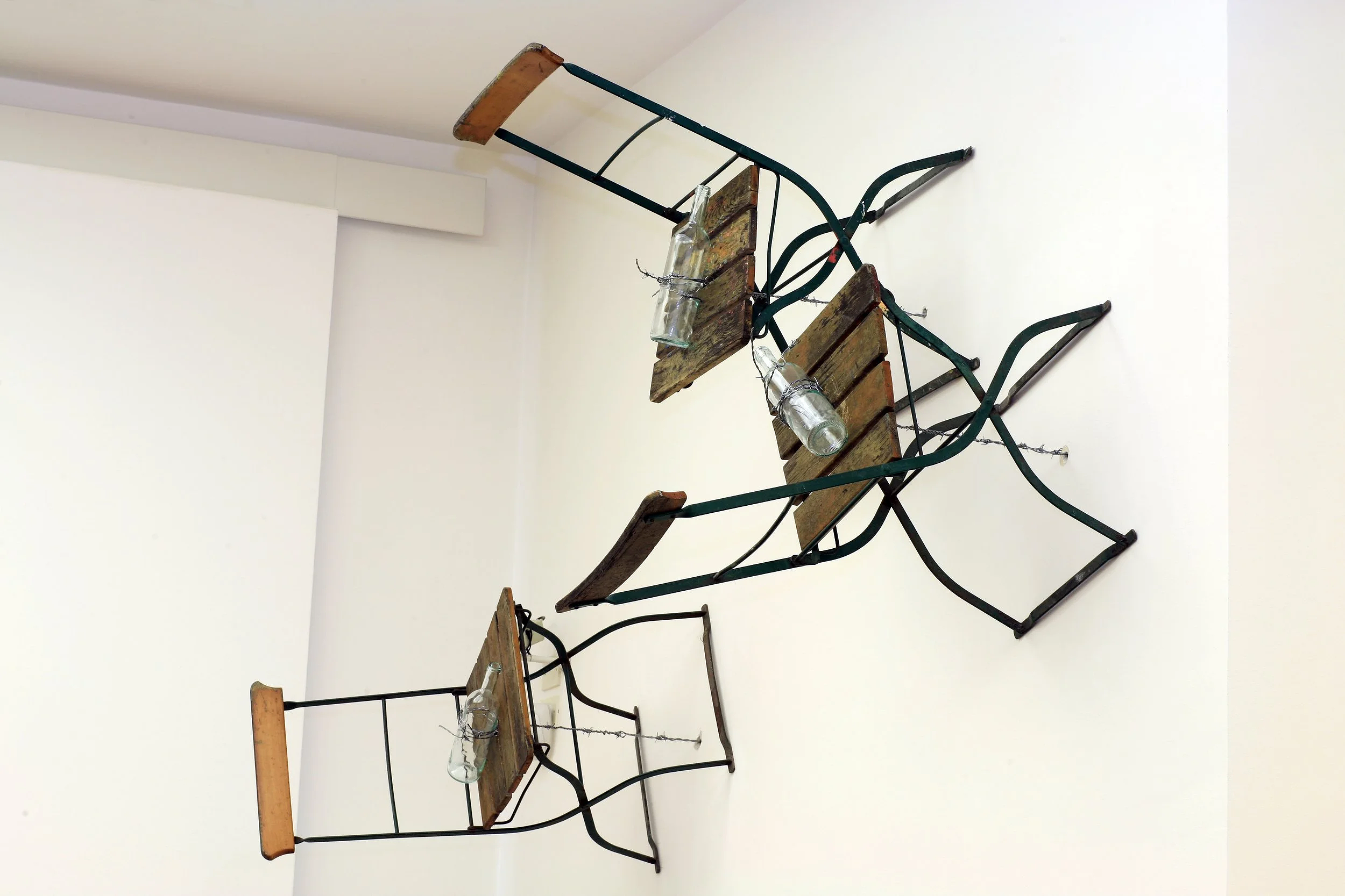 Große Installation, Stühle die durch Stacheldraht der an Flöten/Flaschen befestigt ist und durch die Wand verläuft, vertikal an dieser gehalten werden, Ausstellung vom zeitgenössischen Düsseldorfer Künstler Eduard Winklhofer, in La Spezia 90er Jahre