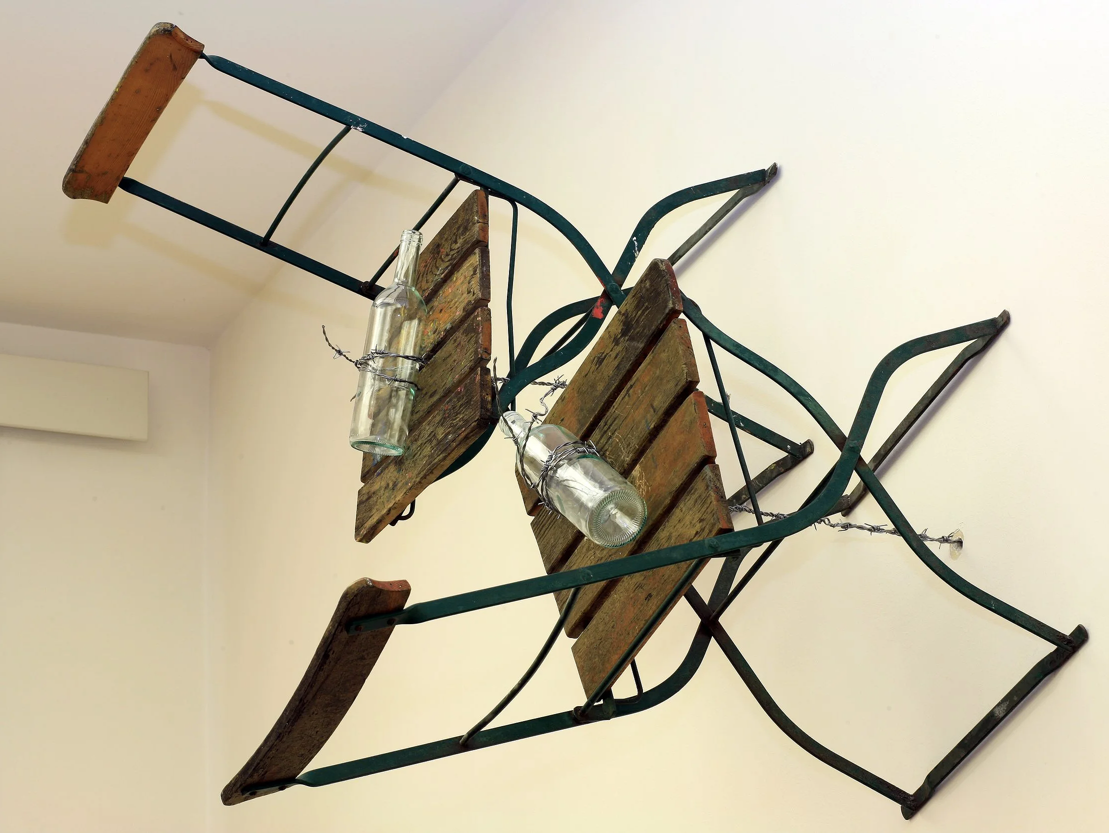 Große Installation, Stühle die durch Stacheldraht der an Flöten/Flaschen befestigt ist und durch die Wand verläuft, vertikal an dieser gehalten werden, Ausstellung vom zeitgenössischen Düsseldorfer Künstler Eduard Winklhofer, in La Spezia 90er Jahre