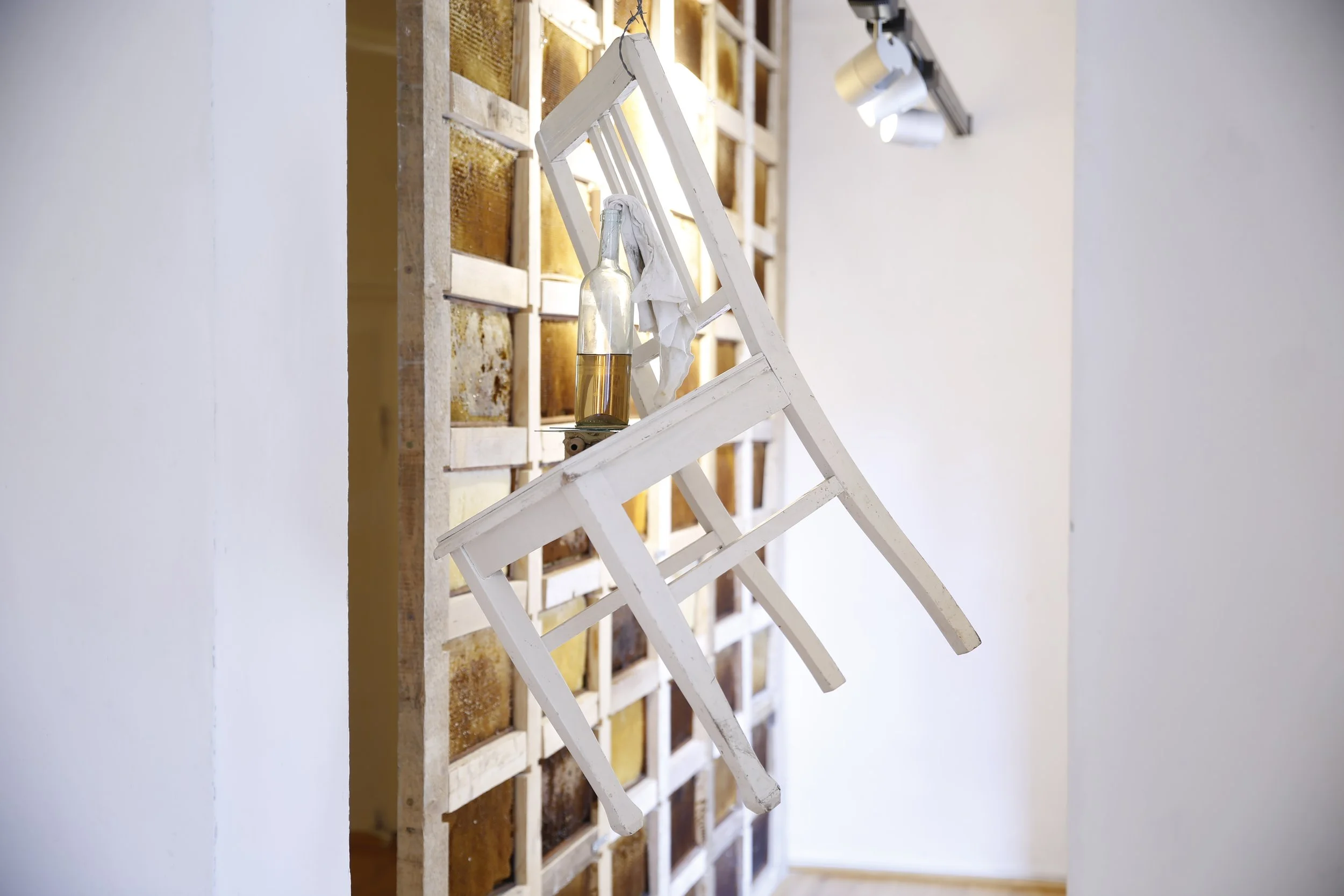 Hängender weißer Stuhl mit Glasflasche und Tuch vor einer Wand aus Bienenwaben, Kunstinstallation, Kulturzentrum bei den Minoriten, Graz, Ausstellung des aktuellen Künstlers Eduard Winklhofer aus Düsseldorf