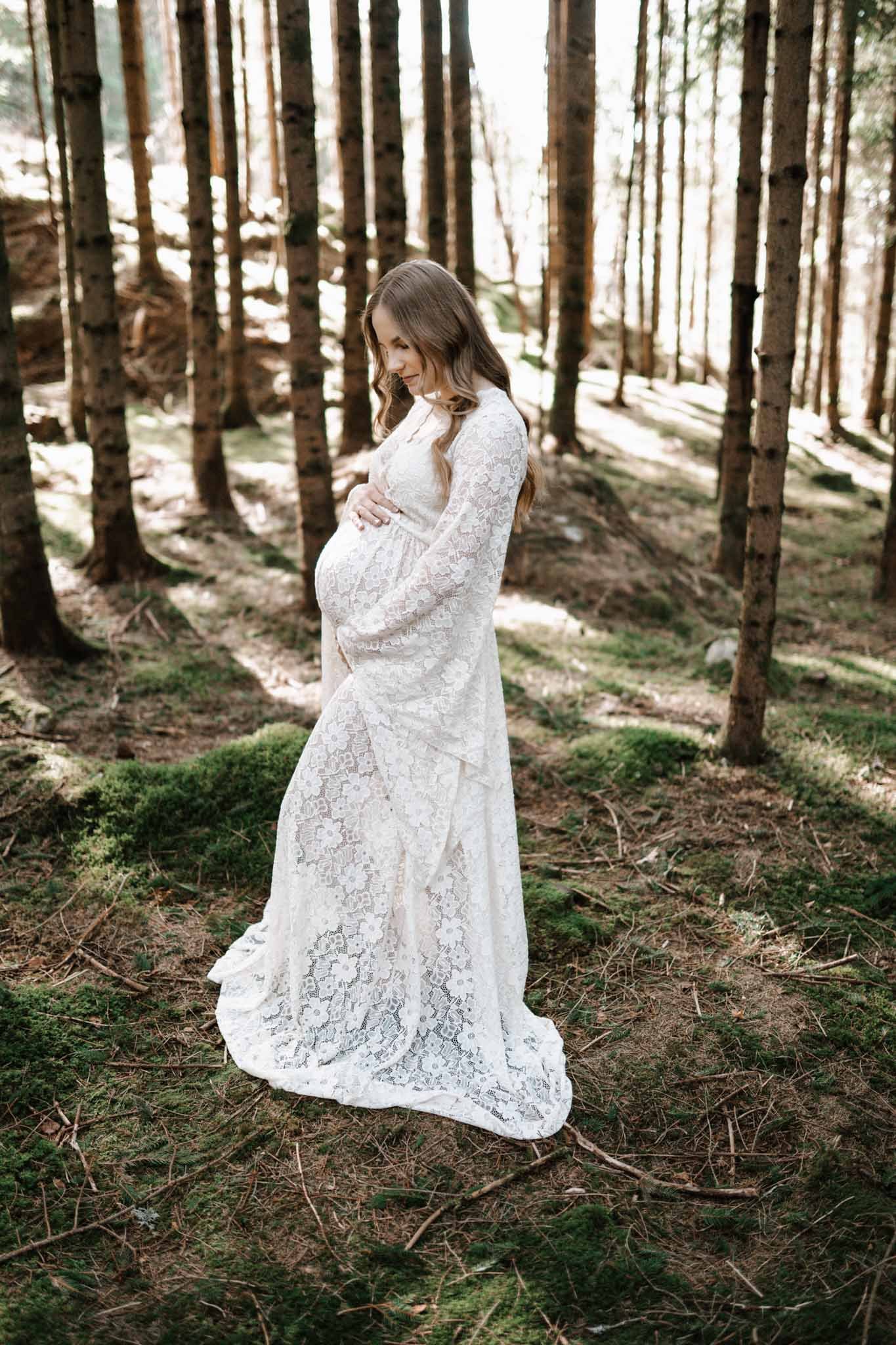 Gravidbilde i skog med nydelige trær. Blondekjole.