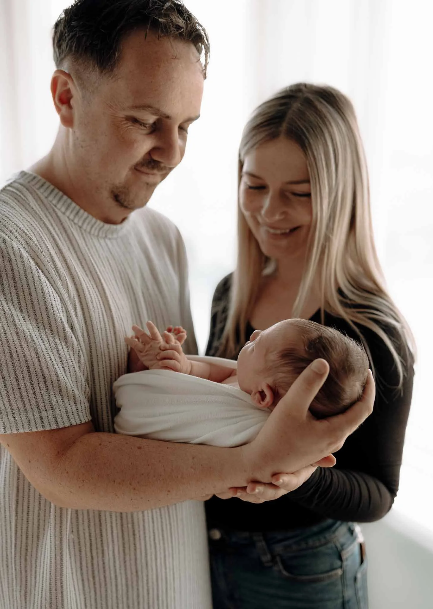 Mor, far og nyfødt baby. Far holder babyen. Ser på han og smiler. 