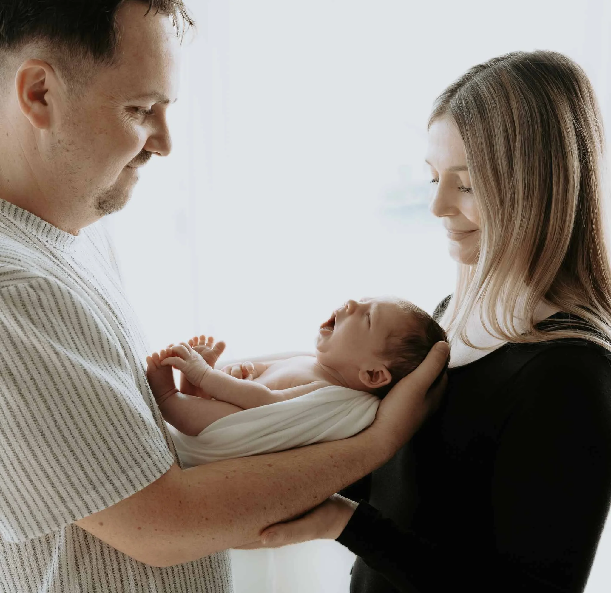 Mor, far og nyfødt baby. Far holder babyen. Ser på han og smiler. 