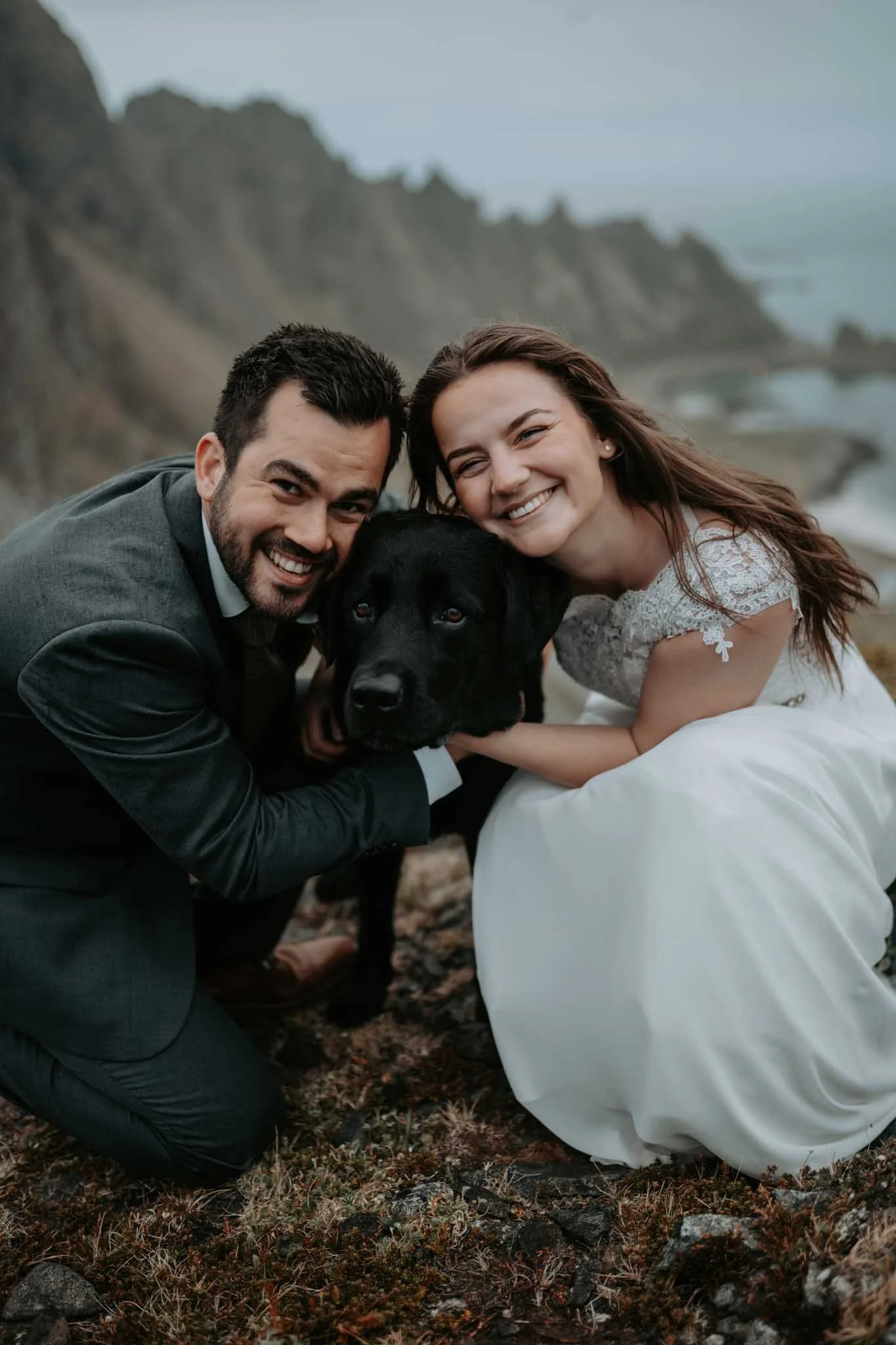 Brudepar smiler og ser på kamera med hunden imellom seg. 