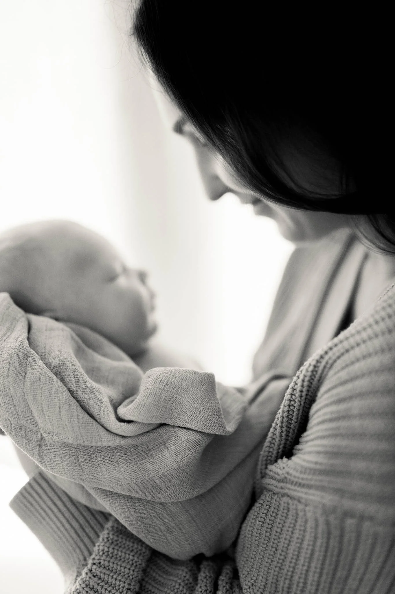 Nærbilde av en kvinne som holder en baby i armene, laget i svart-hvitt.