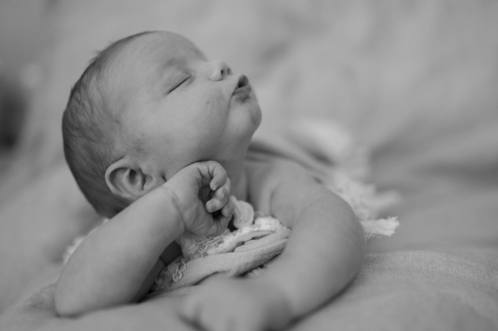 Et svart-hvitt bilde av en sovende baby med lukkede øyne, holdt av en voksen hånd.