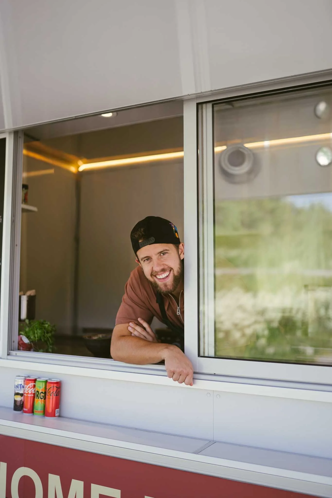 En ung mann står i food trucken å ser ut smilende. 